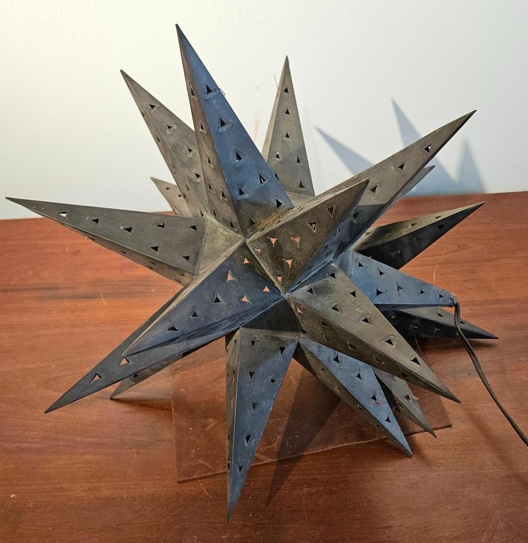 Punched Metal Moravian Star Table Lamp: A table lamp constructed from punched sheet metal in a multi-pointed star form. The body serves as the shade, featuring regular geometric triangular perforations throughout. The metal has an oxidized 