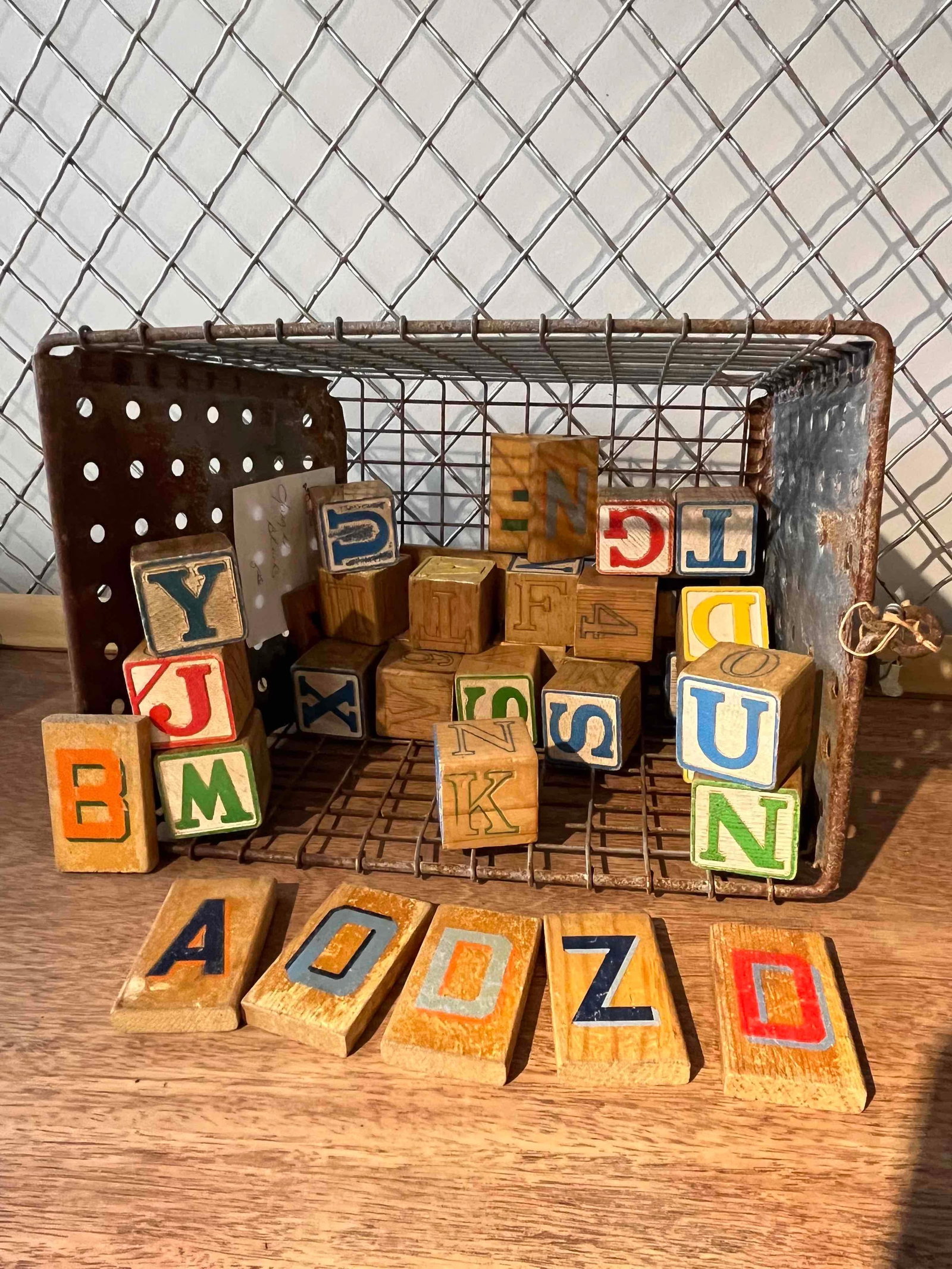 Lyon Metal Basket & Alphabet Blocks: An assortment of wooden toy blocks and a matching industrial metal storage basket. The collection includes cubical blocks and rectangular tiles, featuring natural wood finishes with painted letters, n
