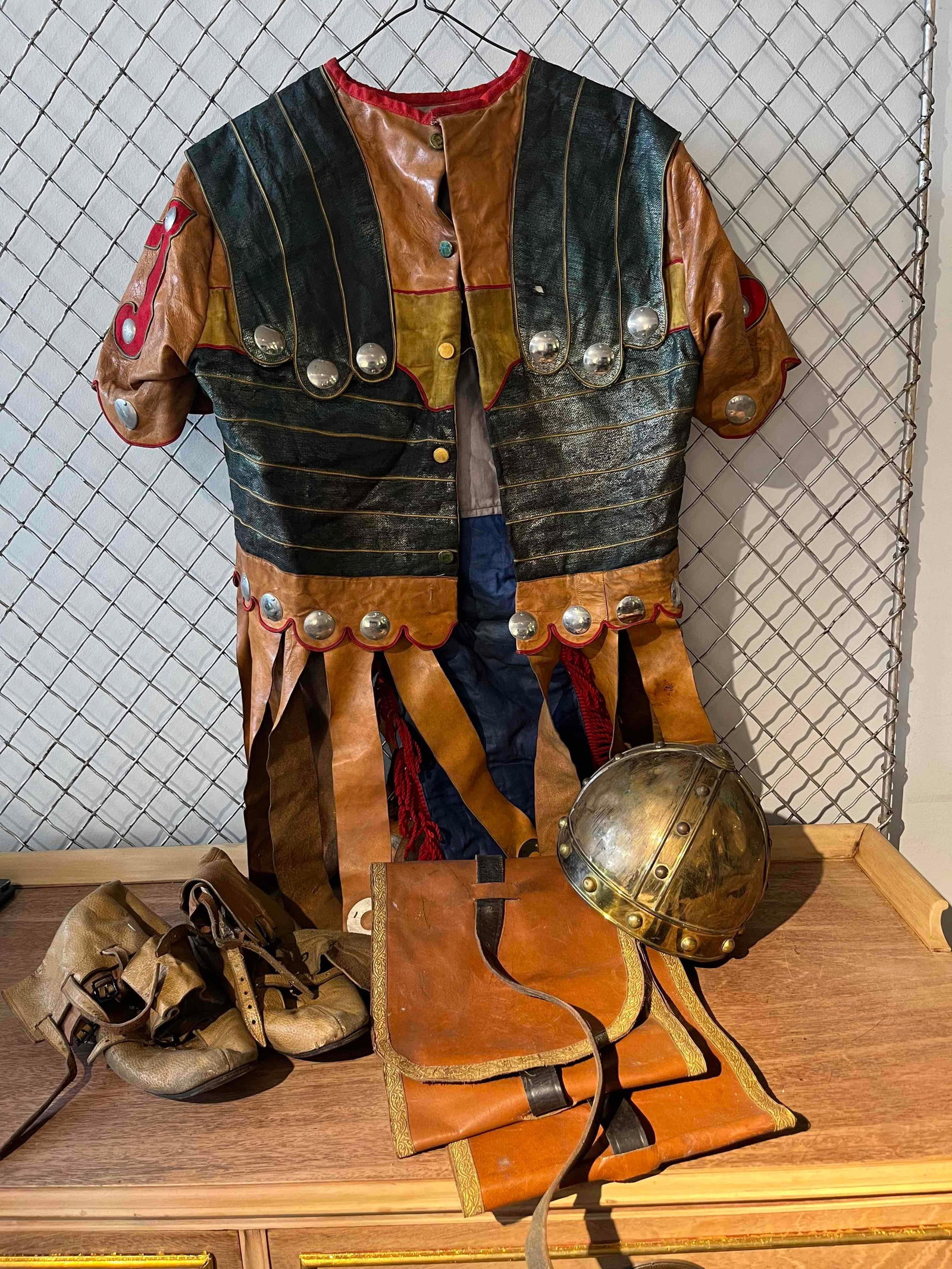 Mid-C. Roman Soldier Costume Components: A set of men's theatrical costume components designed to represent a Roman soldier, including a leather cuirass, a metal helmet, a pair of leather boots, and a decorative leather belt accessory. The c