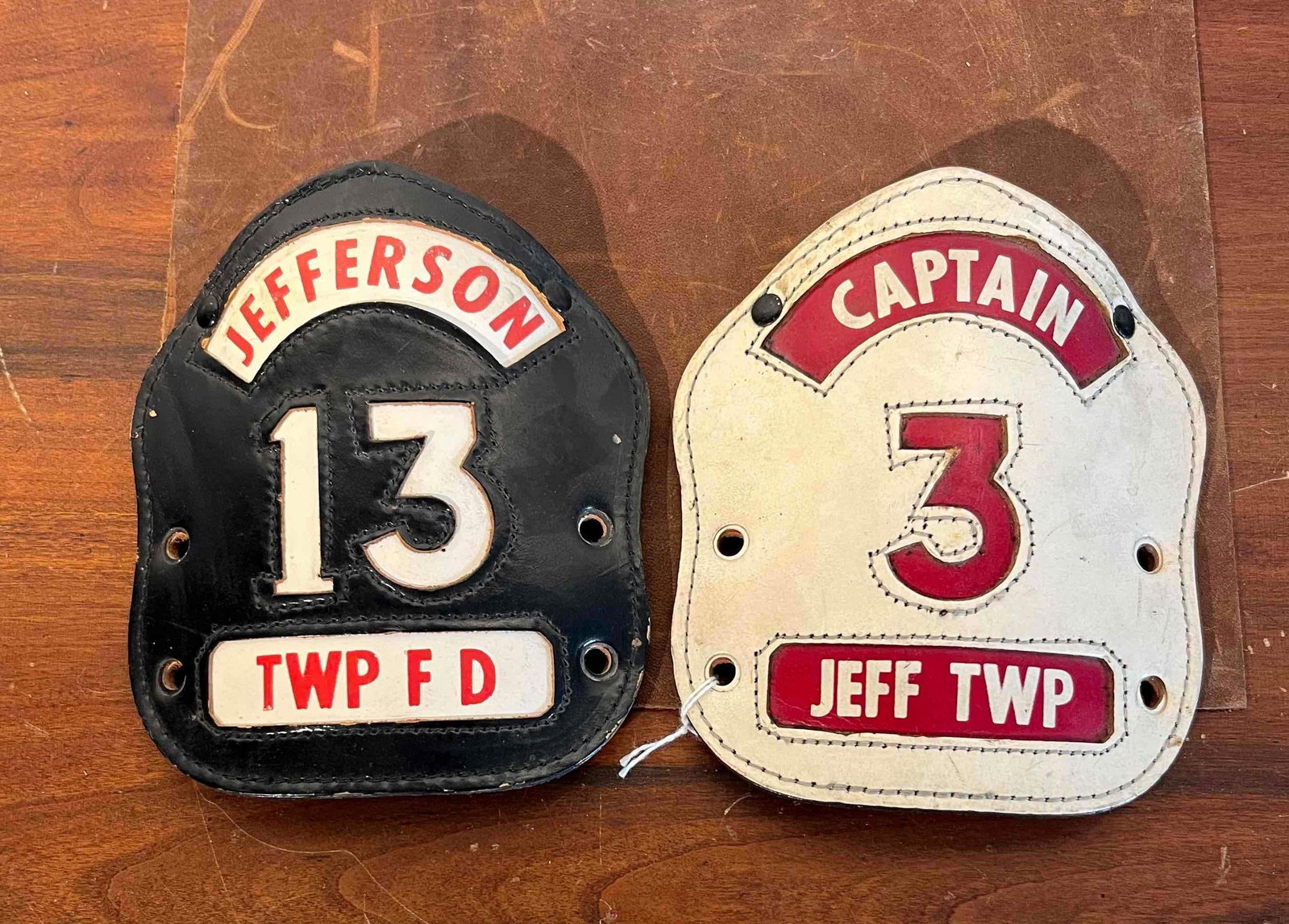 Pair Jefferson Township Helmet Shields: A pair of multi-layered stitched leather fire helmet shields representing Jefferson Township. The first shield is comprised of black leather and features an arched white leather top rocker with red st