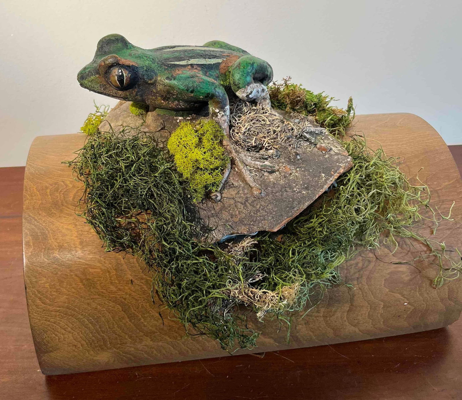 Mixed Media Frog Sculpture, Carved Wood: This mixed media sculpture features a realistic frog figure perched on a naturalistic landscape element, mounted to a substantial wooden support. The frog, rendered with green pigment and three promin