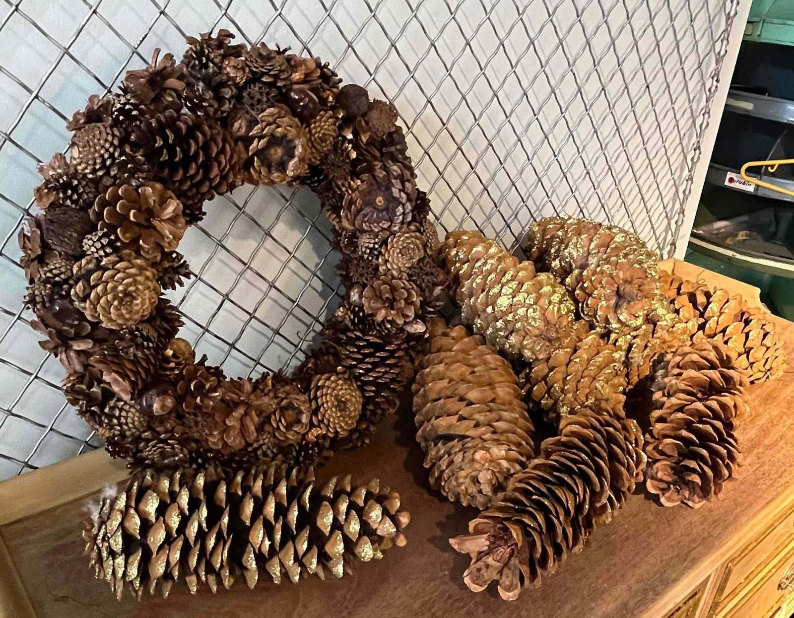 Pinecone Wreath & Specimen Pinecones: An assortment of rustic seasonal decorative items featuring natural botanical specimens. The collection includes one circular wreath and multiple large, elongated specimen pinecones. The wreath is
