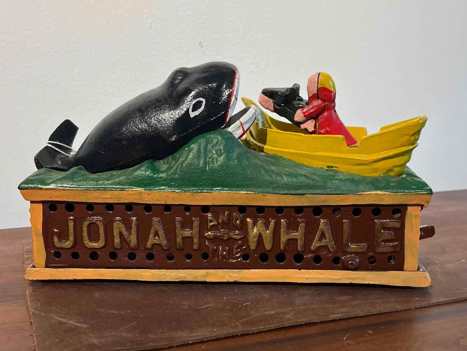Japanese Cast Iron Jonah & Whale Bank: A Japanese cast iron mechanical bank featuring the biblical scene of Jonah and the Whale. The bank is constructed from heavy cast metal and finished with glossy paint. The design consists of a figure 