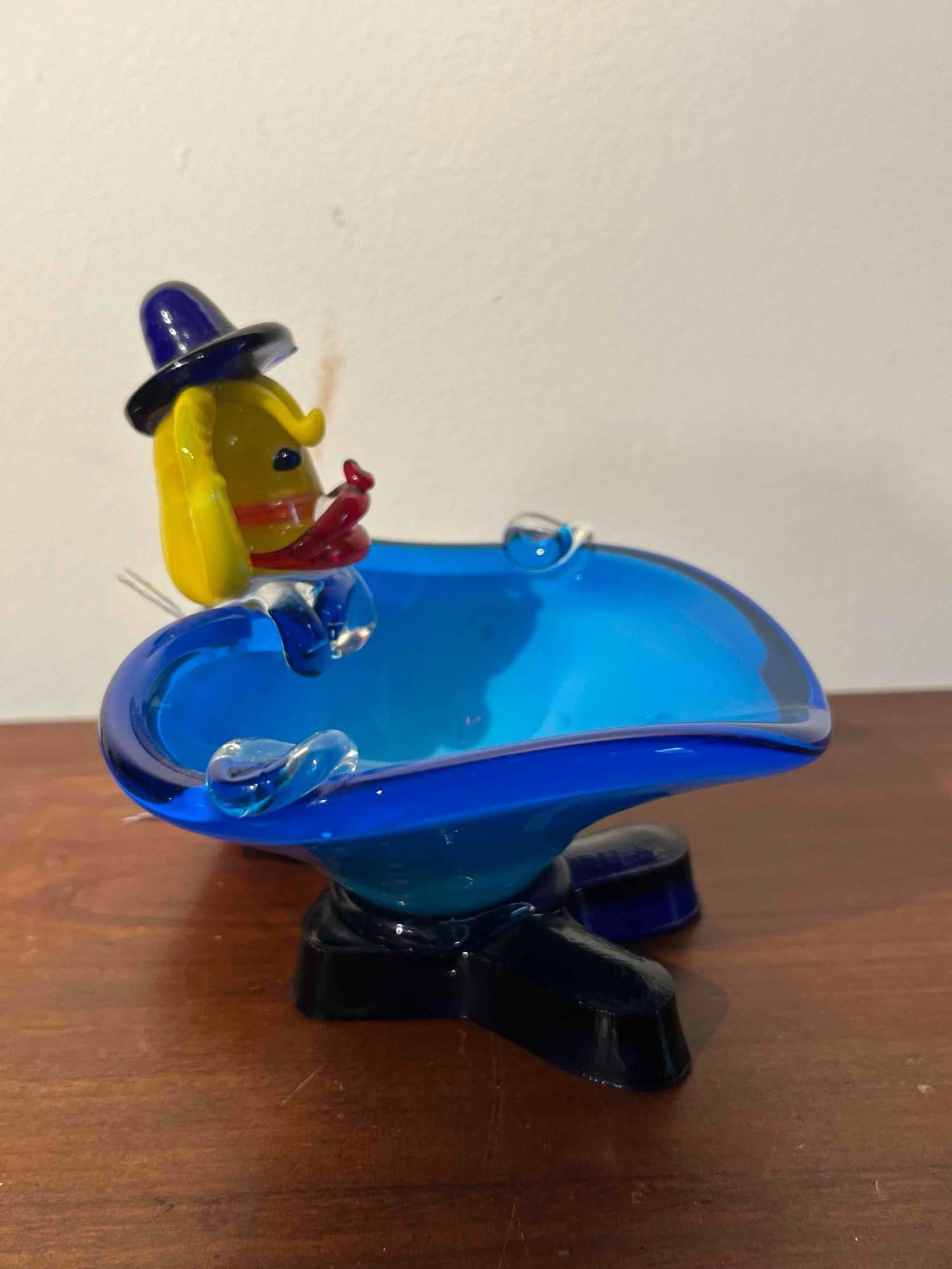 Hand-Blown Art Glass Clown Figural Bowl: Hand-blown art glass decorative vessel featuring a stylized clown figure integrated into the rim. The piece is constructed with a translucent vibrant blue glass bowl and two applied clear glass rests.