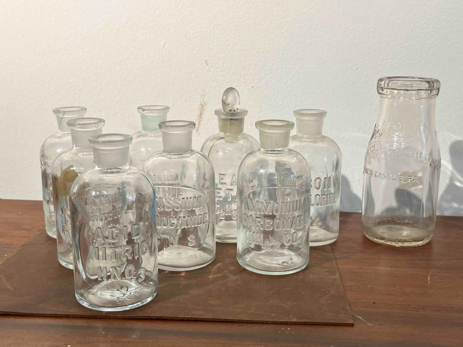 9 T.C. Wheaton & Wester's Glass Bottles: This collection consists of nine clear glass bottles, including eight laboratory reagent bottles and one dairy bottle. The reagent bottles are constructed of mold-blown clear glass with cylindrical bo