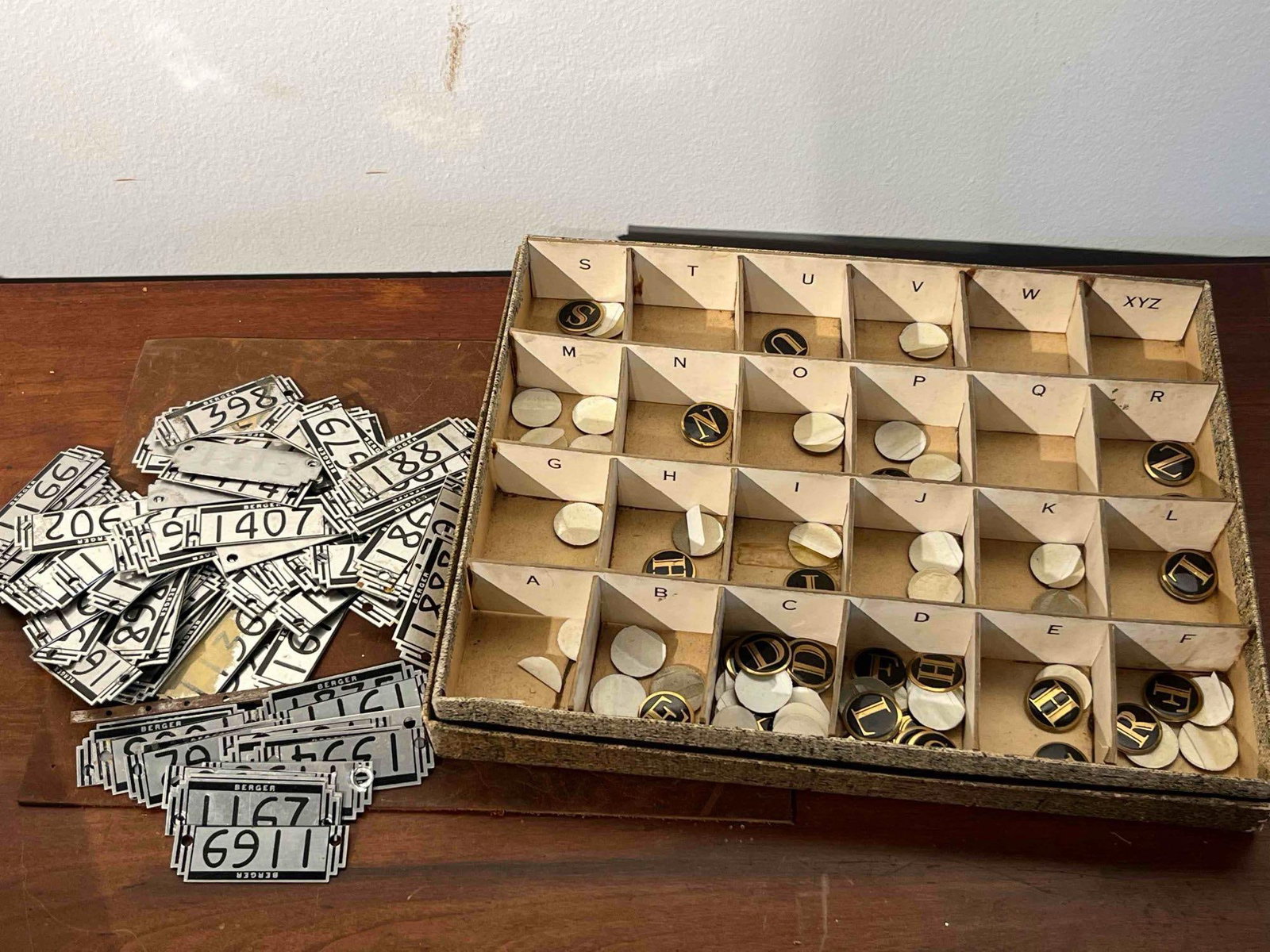 Berger Metal Locker Plates & Monograms: A group of industrial identification hardware including a bulk lot of numbered metal plates and a partitioned tray of adhesive monogram letters. The metal plates feature an Art Deco stepped geometric 