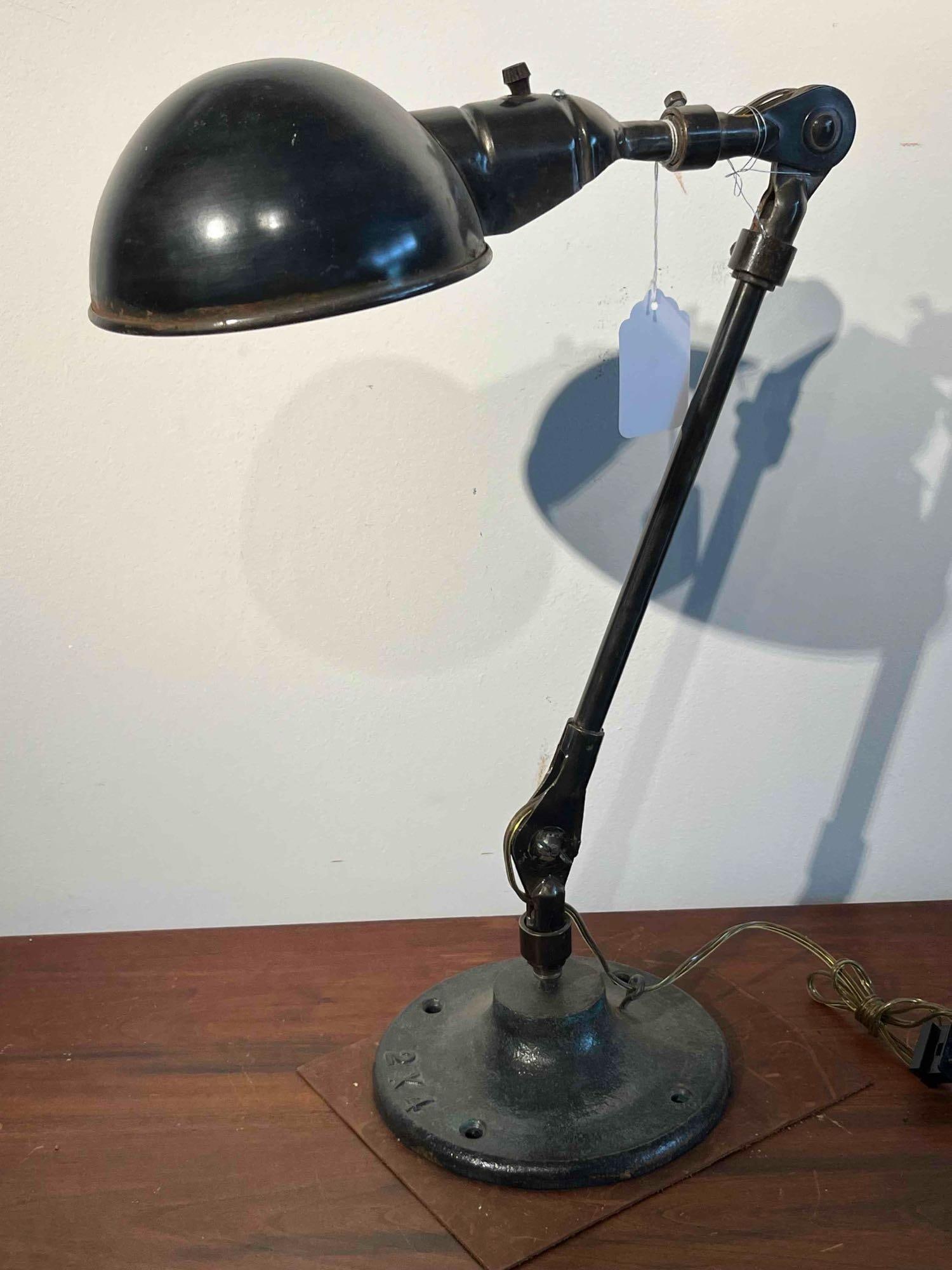 Articulated Task Lamp w/ Cast Iron Base: An industrial-style articulated task lamp featuring a two-part adjustable arm and a circular cast-iron flange base. The lamp is constructed with tubular metal segments connected by adjustable