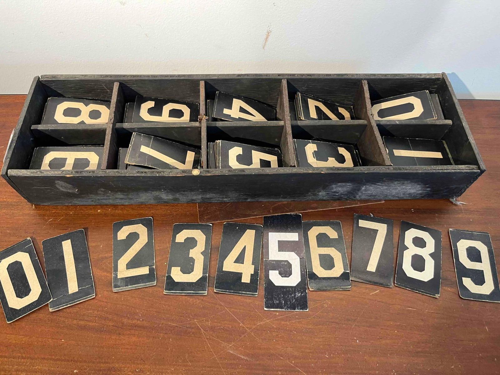 Number Cards in Divided Wood Crate: A collection of printed number cards housed in a custom-compartmentalized wooden storage box. The set comprises multiple copies of digits ranging from 0 to 9, featuring a bold, cream-colored block fon