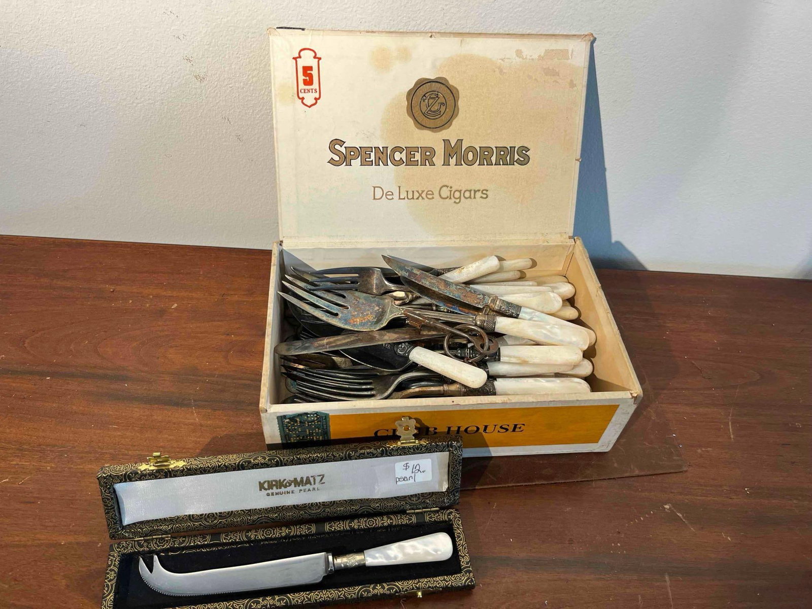 Mother-of-Pearl Flatware w/ Kirk & Matz: This collection consists of a boxed cheese knife and an assortment of loose flatware, all featuring mother-of-pearl handles. The boxed item is an individual cheese knife with a serrated blade and