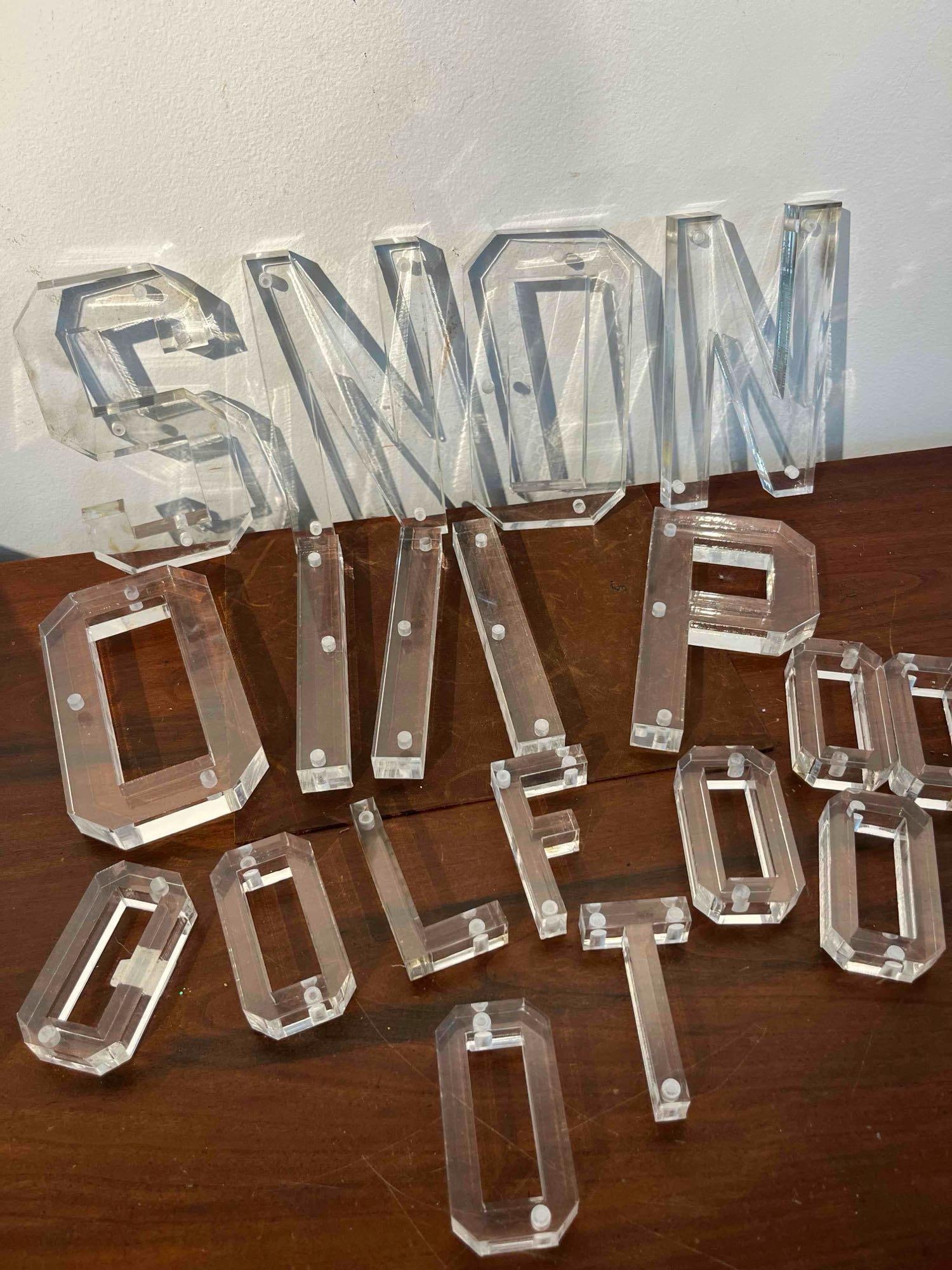 18 Dimensional Acrylic Sign Letters: A collection of eighteen dimensional sign letters and components crafted from thick, clear polished acrylic. The letters feature a bold, block-style font with beveled edges and integrated clear
