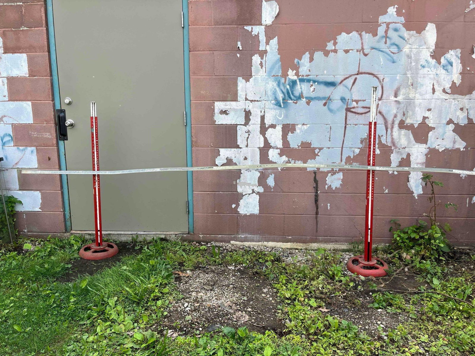Pair Telescoping High Jump Standards: A pair of track and field high jump standards accompanied by a matching crossbar. The standards are constructed from square-profile metal tubing finished in red and white paint and are mounted to