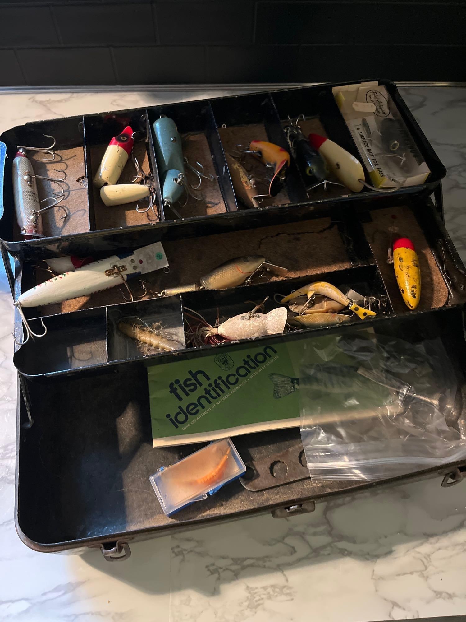 Heddon & Fred Arbogast Lures & Box: An assortment of fishing equipment featuring a metal tackle box and a variety of lures and associated ephemera. The single-tray cantilever tackle box is constructed of steel with a dark green or
