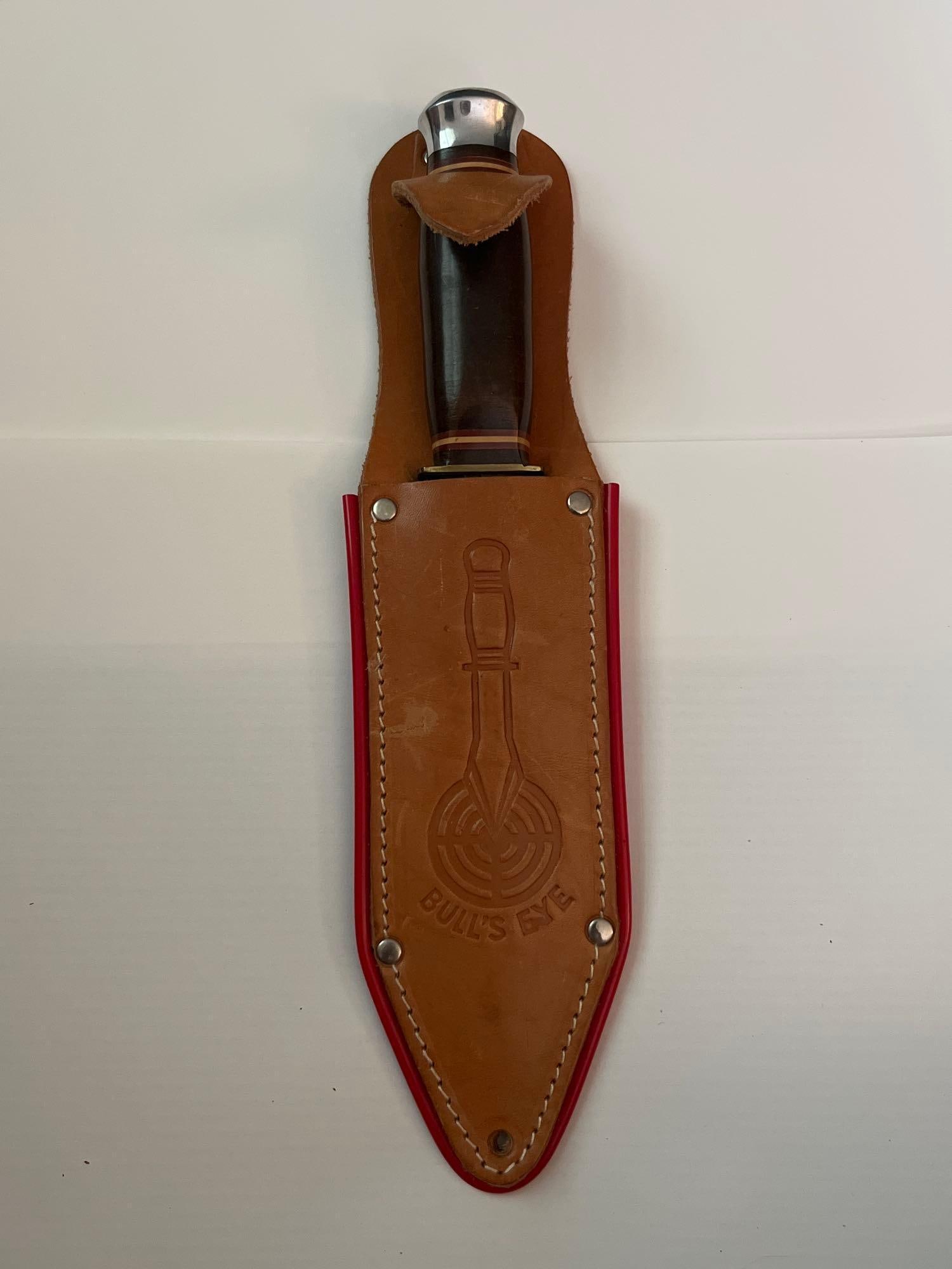 German Throwing Knife & Sheath: A German-made fixed-blade throwing knife featuring a double-edged spear-point blade of polished steel. The handle is constructed with stacked dark brown composite or leather washers, accented by decor