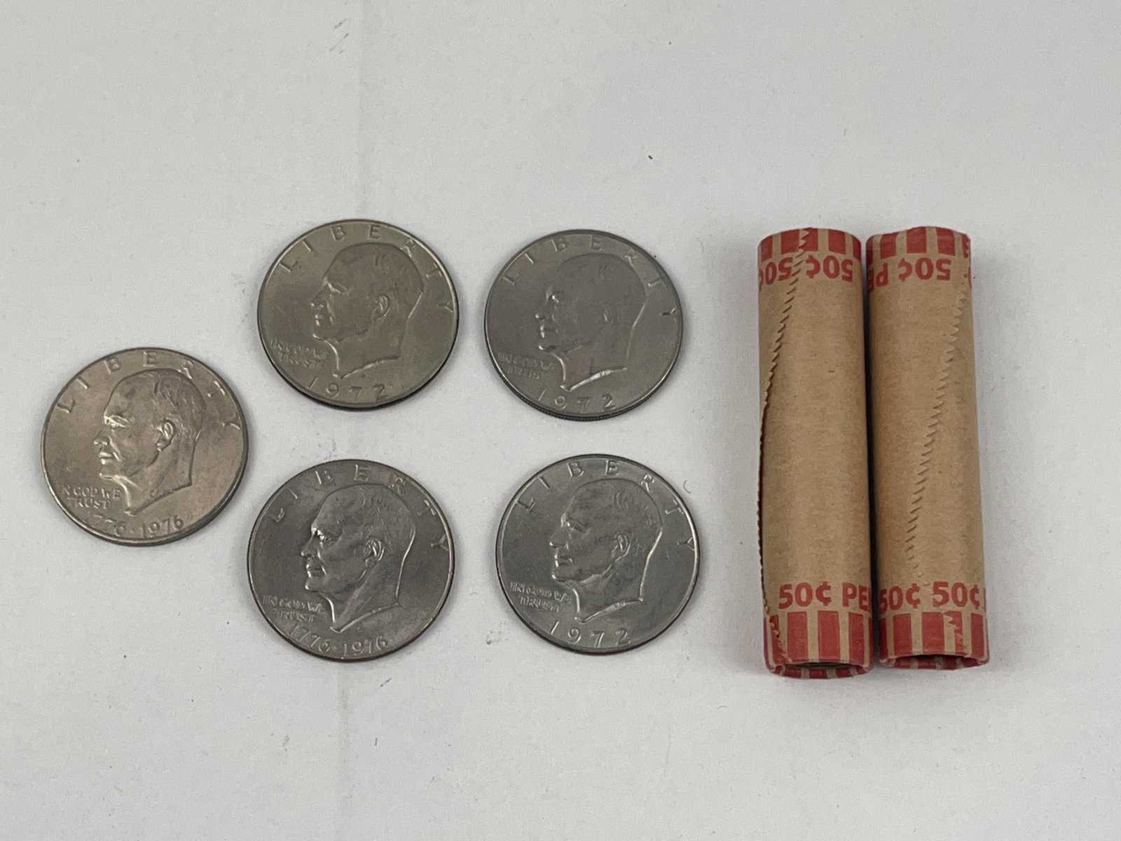 US Eisenhower Dollars & Rolled Pennies: A collection of US currency consisting of Eisenhower One Dollar coins and two paper-wrapped rolls of pennies. The group includes two 1776-1976 Bicentennial commemorative Eisenhower dollars, featuring 