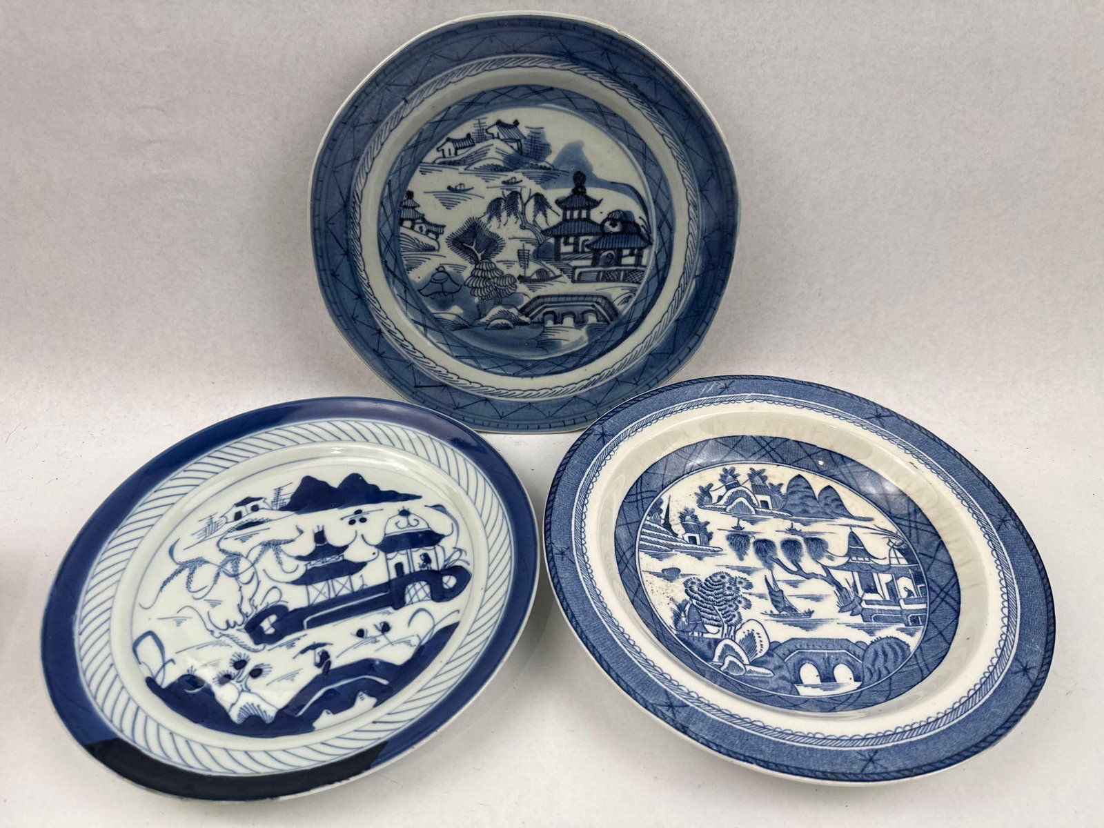 Trio Blue & White Chinese & Wood Plates: This lot features three assorted blue and white ceramic plates of varied origins. The first is a hand-painted porcelain plate decorated in a traditional Canton style landscape. Item 2 (Marked China): 