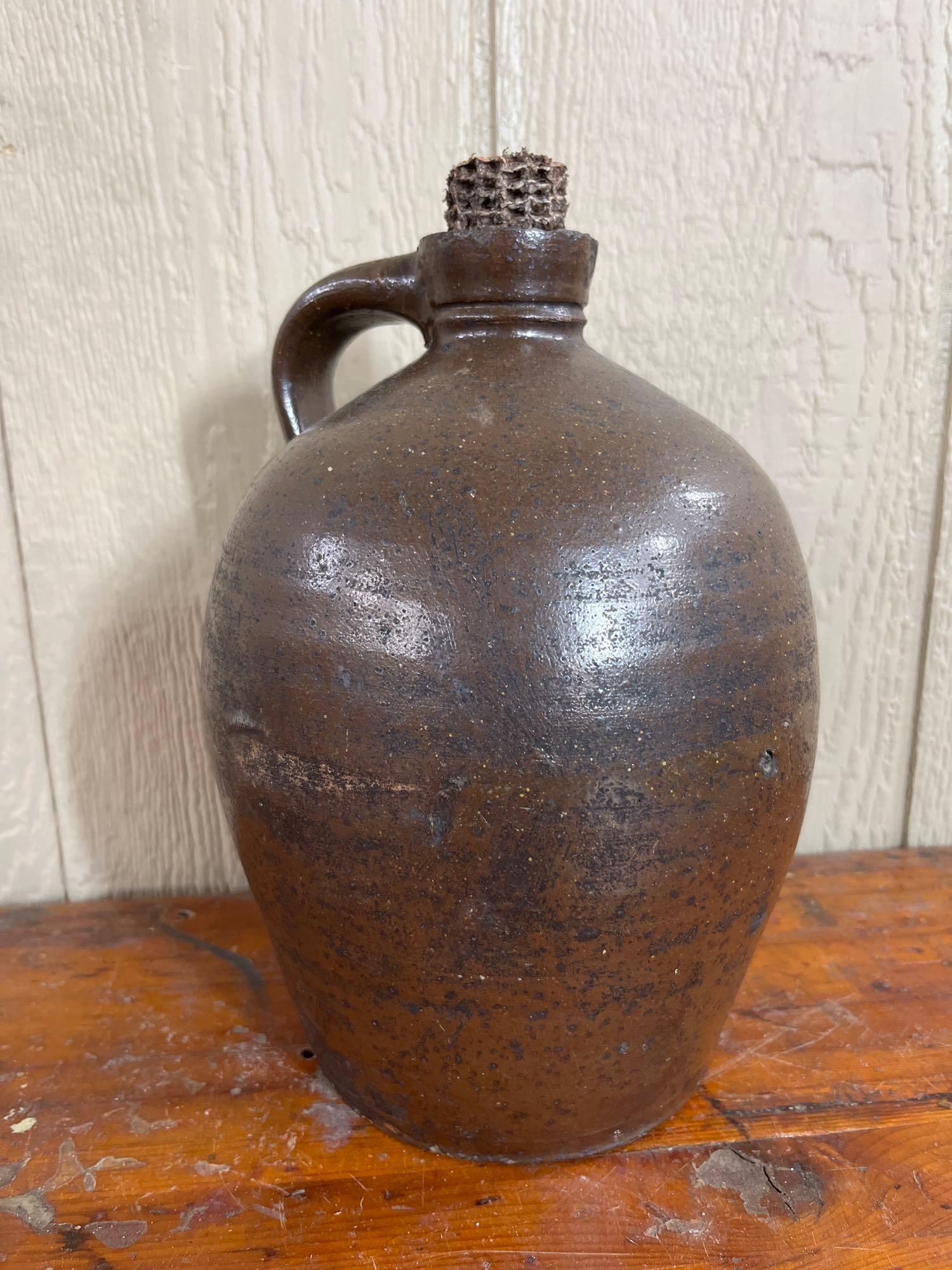 American Albany Slip Stoneware Jug: An American stoneware jug of utilitarian form, dating to the mid-to-late 19th century. The vessel features a classic ovoid body that tapers toward a flat, circular base. No maker marks, signatures,