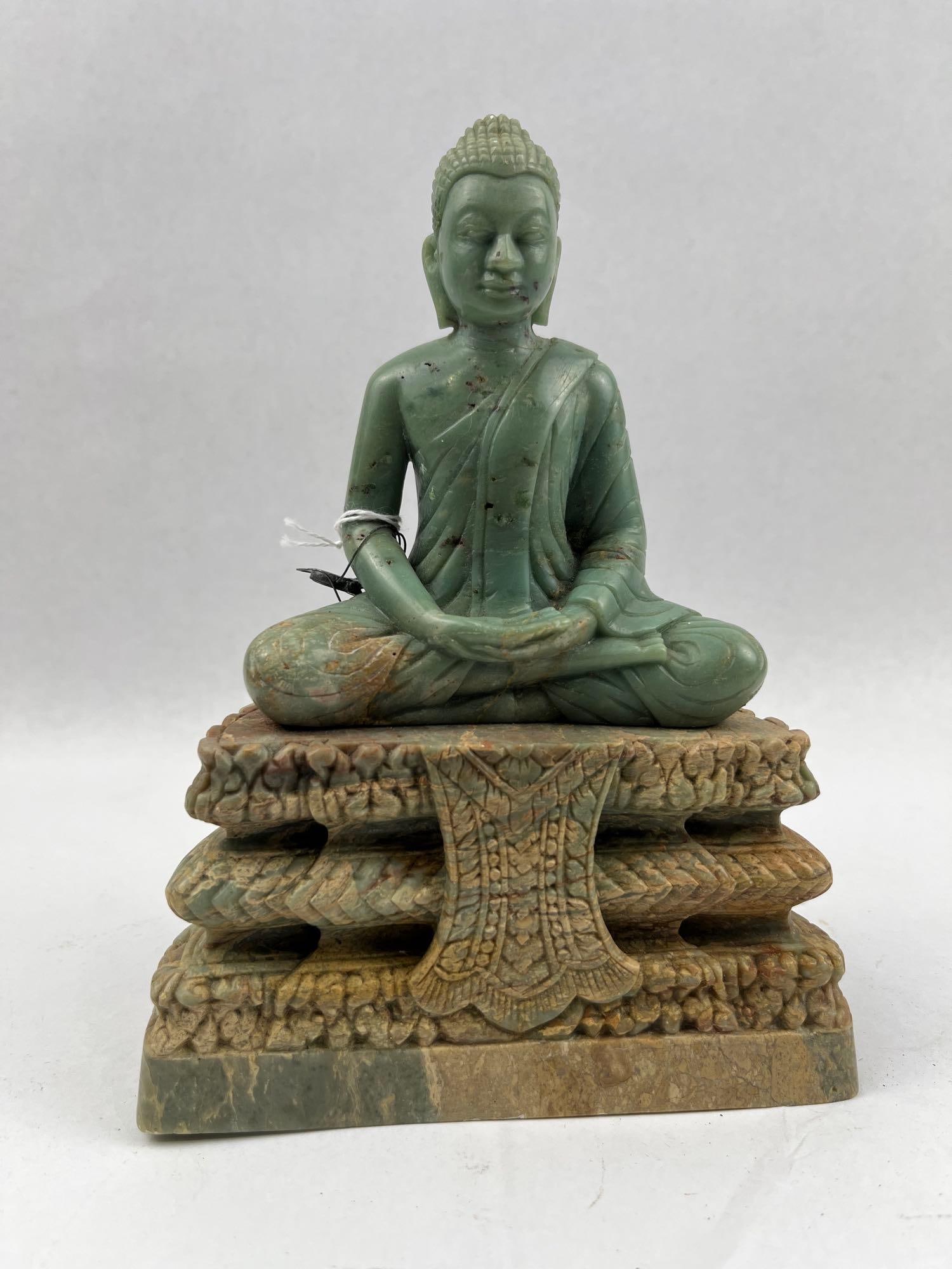 Southeast Asian Seated Stone Buddha: A carved variegated green stone statue depicting a seated Buddha. The Buddha is seated upon a high, three-tiered ornate base which features a central decorative apron or cloth element hanging down