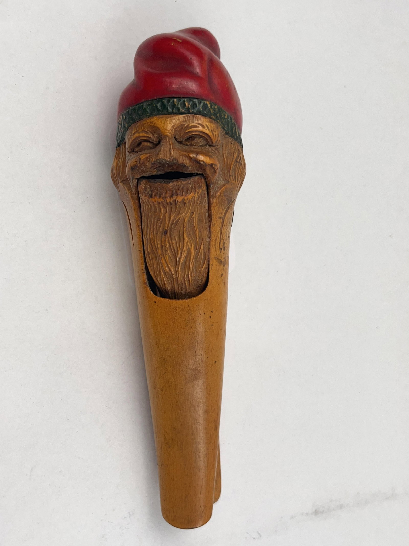 Hand-Carved Wooden Gnome Nutcracker: A hand-carved wooden lever-action nutcracker crafted from hardwood. The facial features, including narrowed eyes and a wide, open mouth, are rendered with detailed carving, while the long beard and