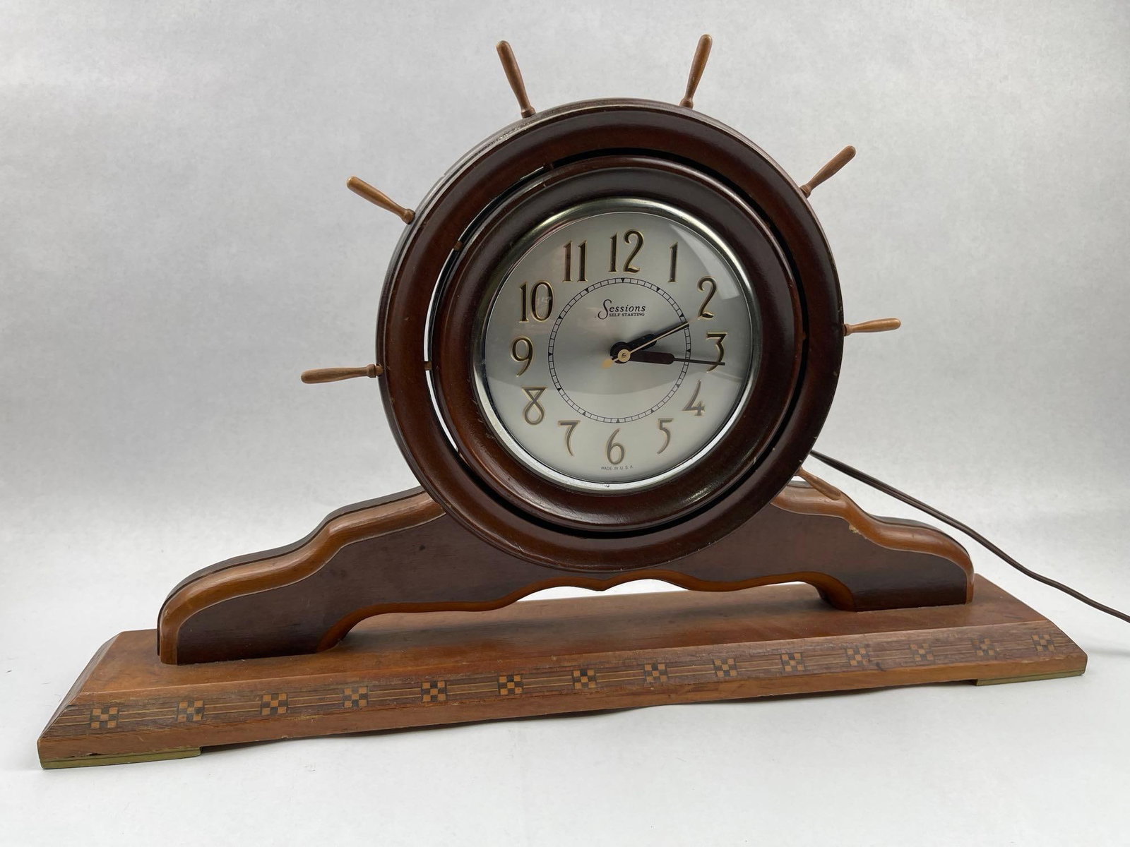 Sessions Ship Wheel Mantel Clock: An American-made electric mantel clock by the Sessions Clock Company, featuring a nautical ship wheel design. The clock is housed in a circular wooden frame with eight projecting wooden spokes, mounte