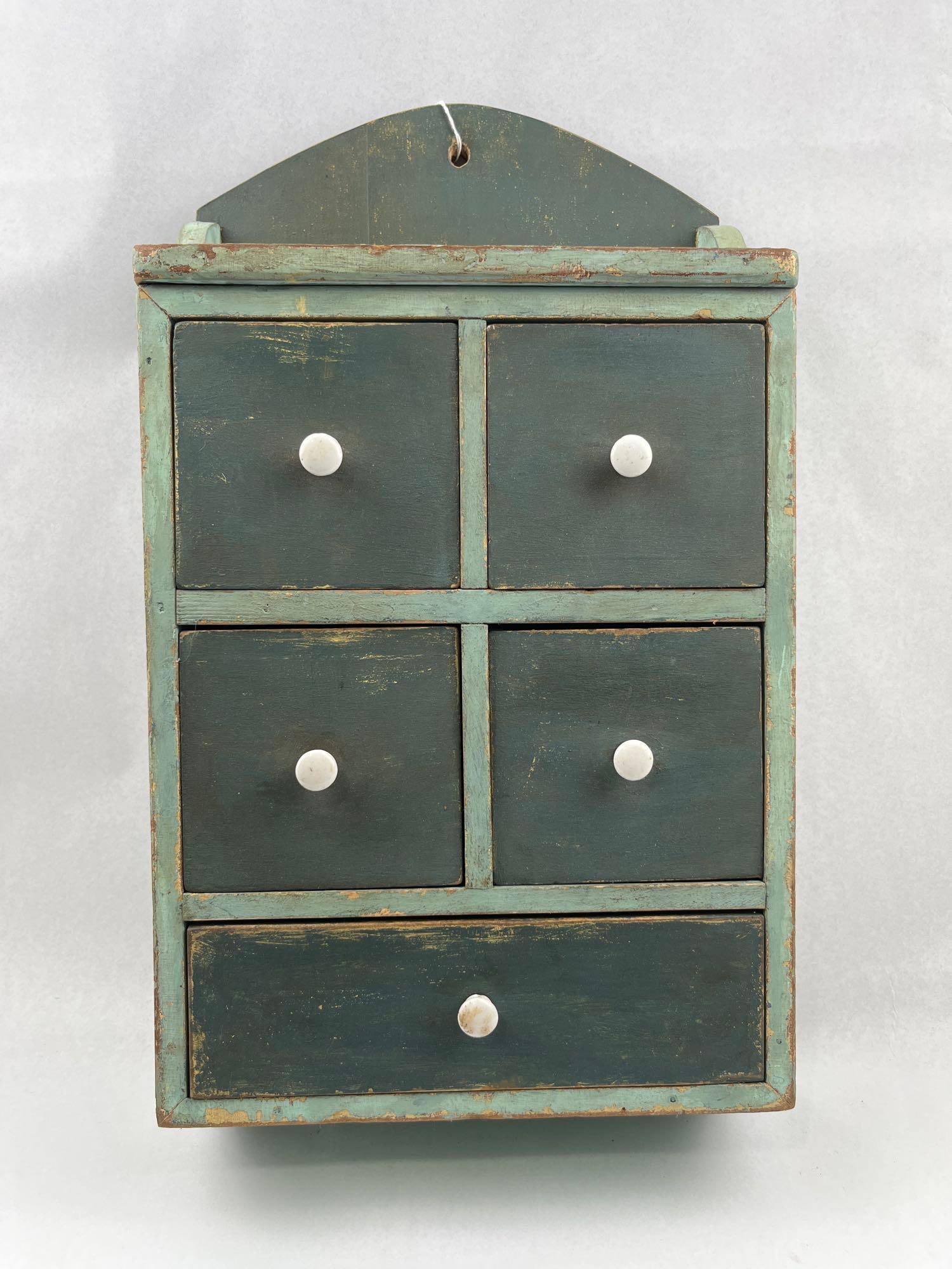 American Primitive 5-Drawer Spice Chest: This miniature wall-hanging chest is designed in the American Primitive style, featuring a rectangular frame with a shaped backsplash and five drawers. The construction consists of a solid wood frame