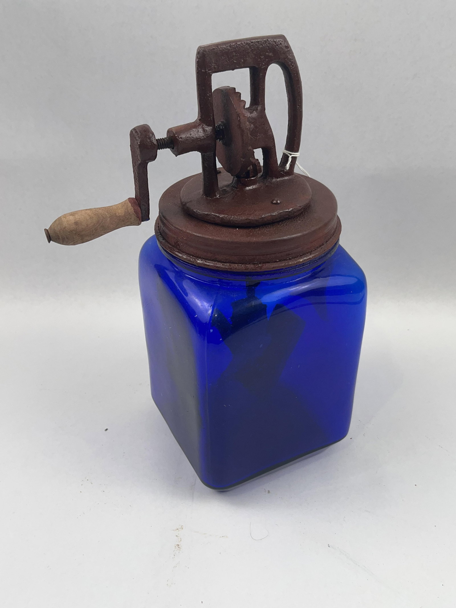 Dazey No 20 Cobalt Glass Butter Churn: A hand-cranked butter churn manufactured by the Dazey Churn and Manufacturing Company. The item consists of a square-profile cobalt blue glass jar and a cast iron mechanical lid assembly. The front