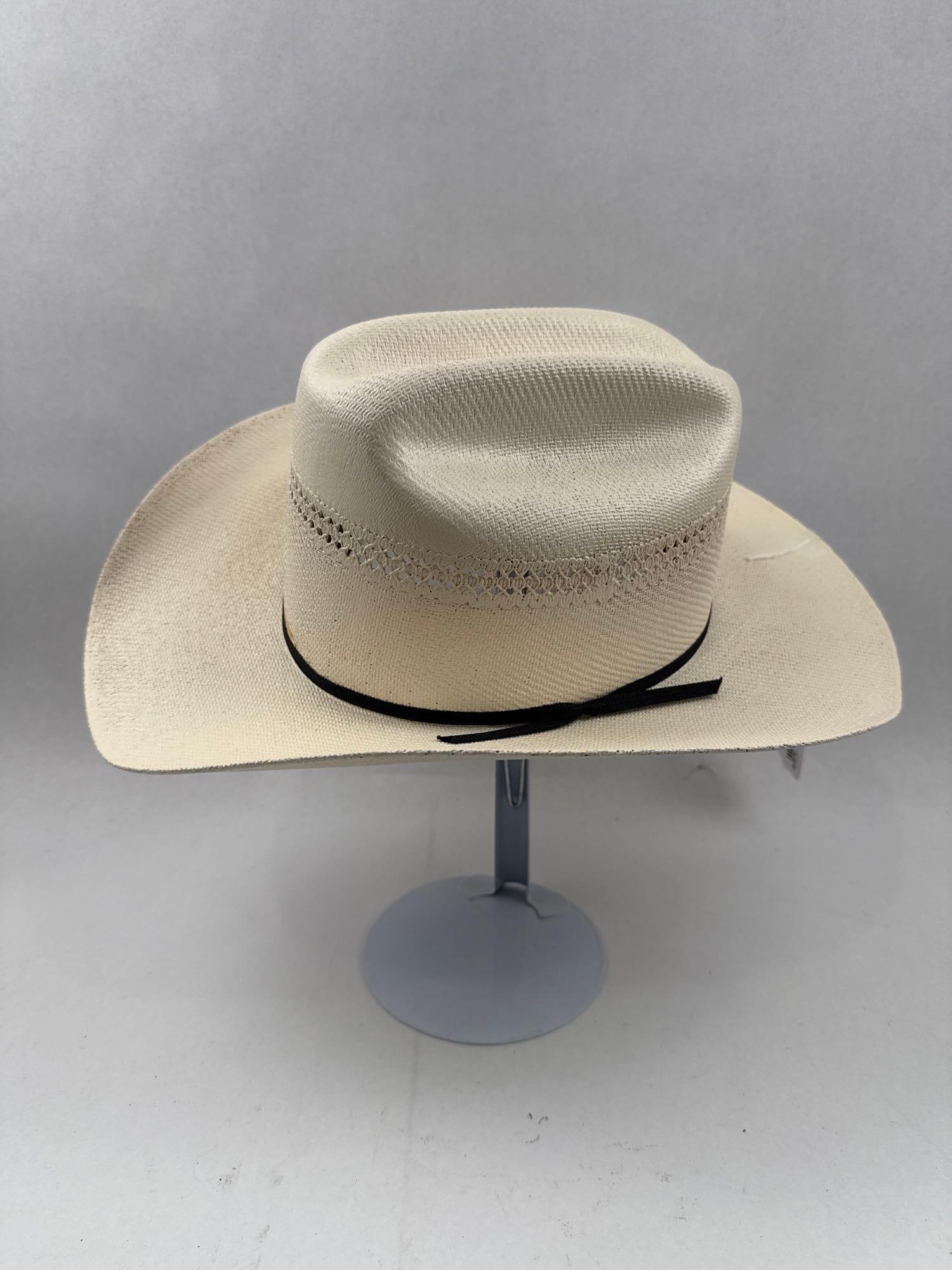 Woven Straw Cattleman Crease Cowboy Hat: A cream-colored woven straw cowboy hat featuring a classic cattleman crease crown. It is finished with a narrow black fabric ribbon hatband that is tied in a small bow on the left side. A white fabric