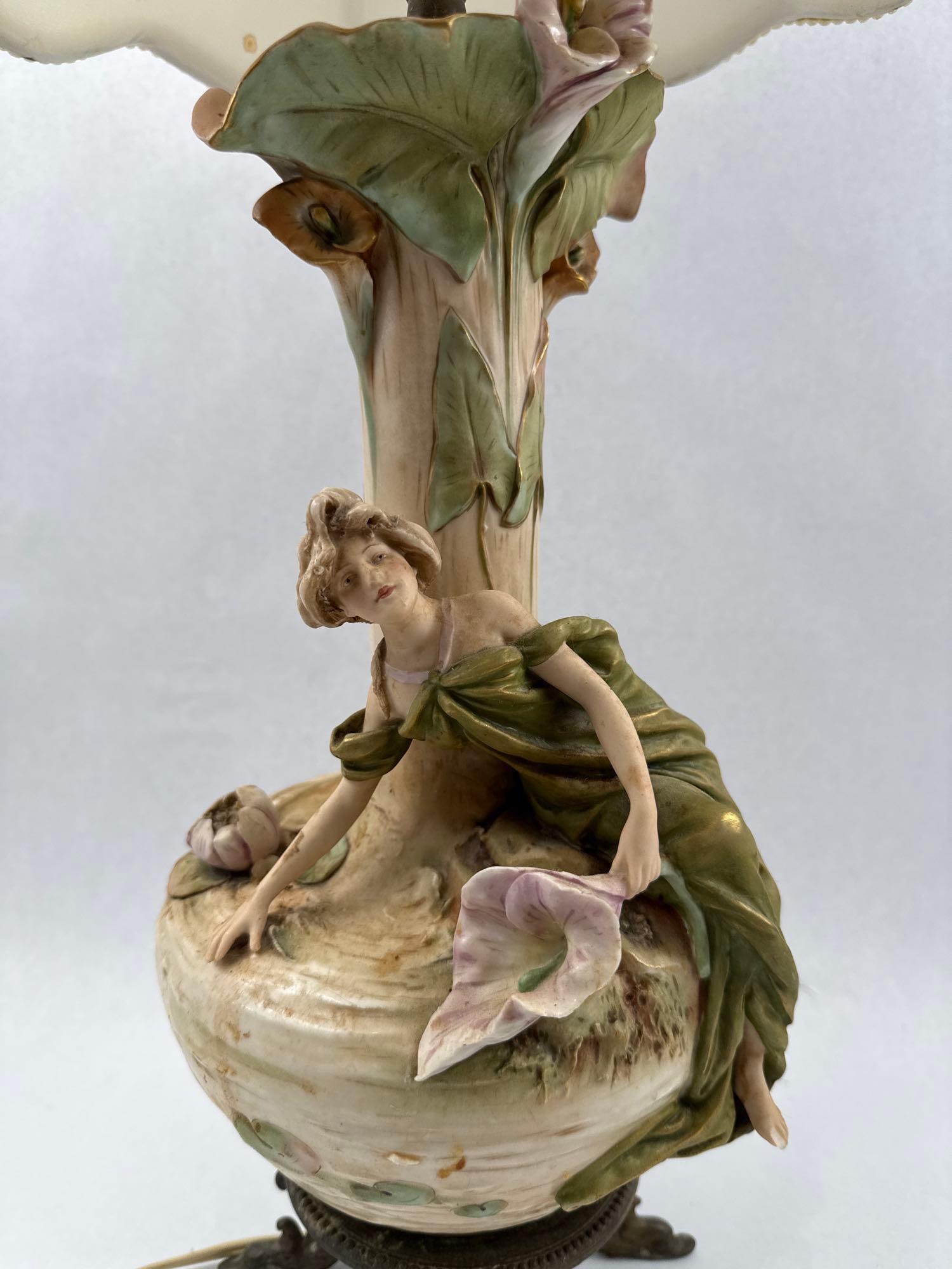 Art Nouveau Porc. Nymph & Lily Lamp: A table lamp featuring a hand-painted matte-glazed bisque porcelain body set on a cast metal base. The porcelain component is mounted on a circular cast metal stand with a beaded top rim, supported by