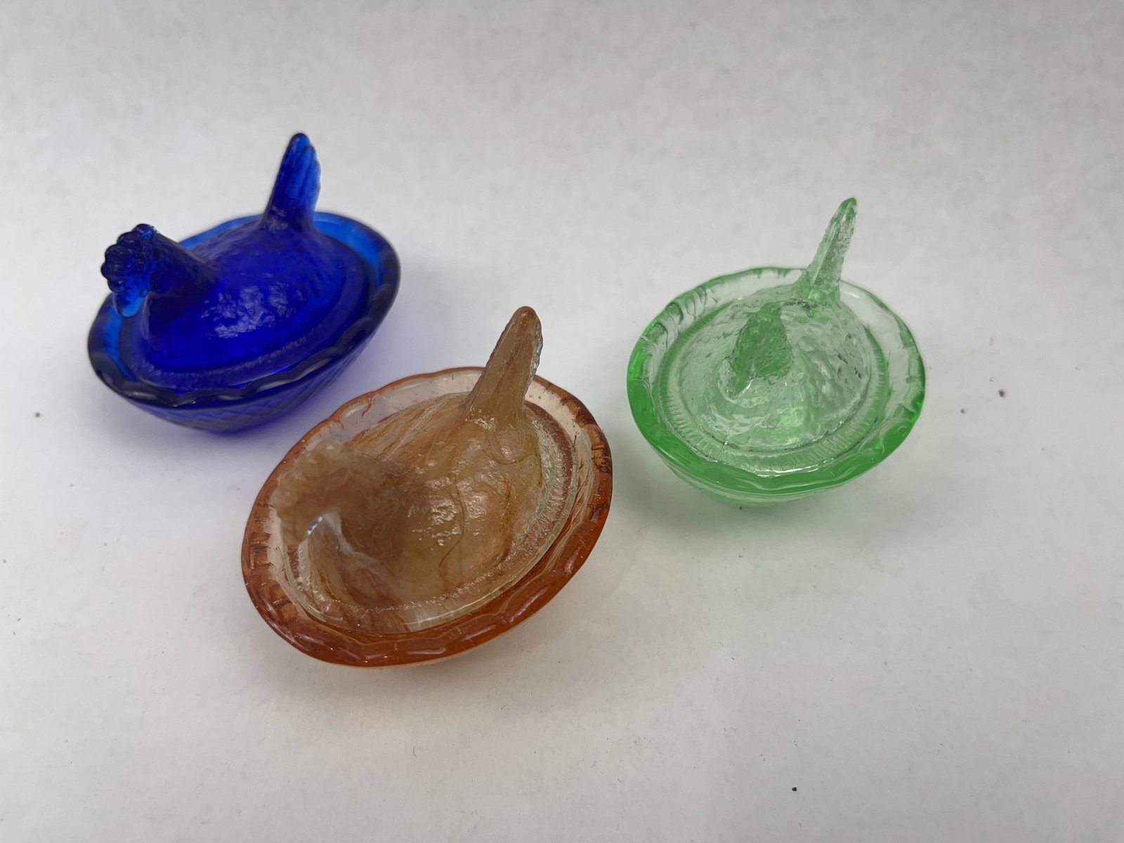 Three Pressed Glass Hen on Nest Dishes: A trio of miniature two-part pressed glass covered dishes, designed in the form of a hen on a nest. Each piece consists of a figural lid shaped like a brooding hen with molded feather textures and a