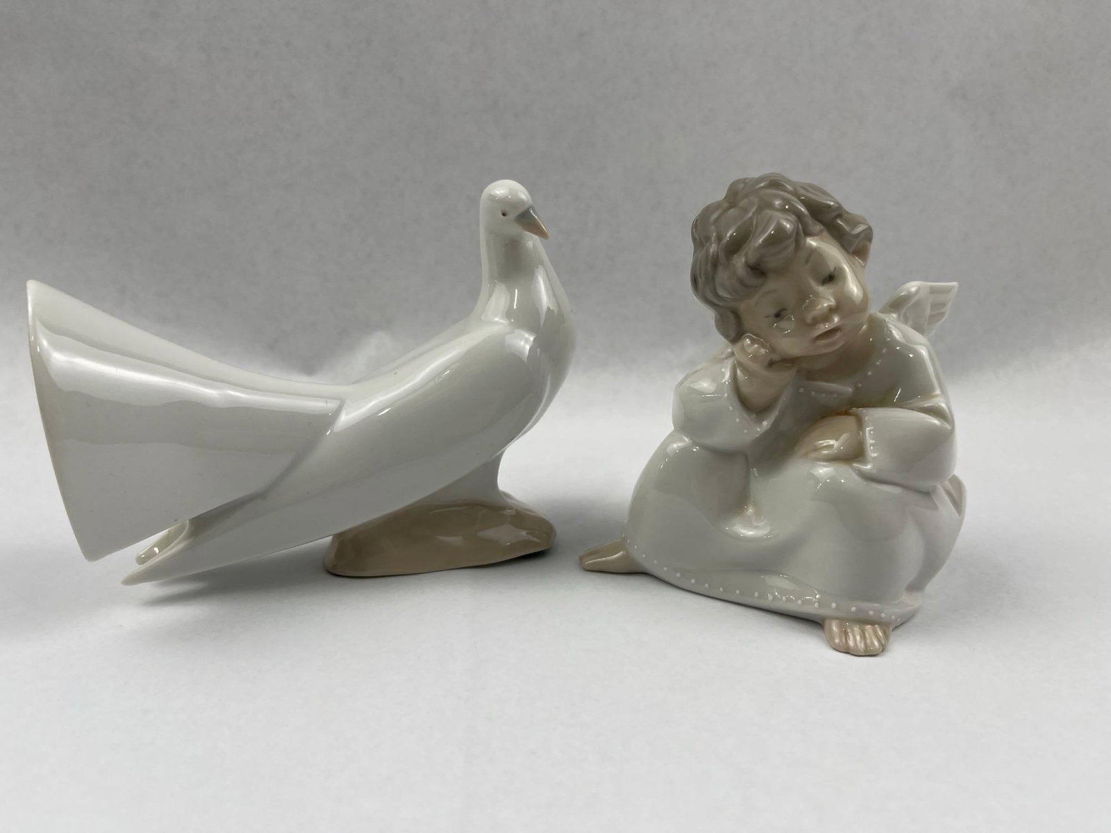 Pair Lladro Spanish Porc. Figurines: This pair of Spanish glazed porcelain figurines comprises two distinct animal and human studies. The second figure is a fan-tail dove or pigeon modeled with a broad, upright tail and standing on a
