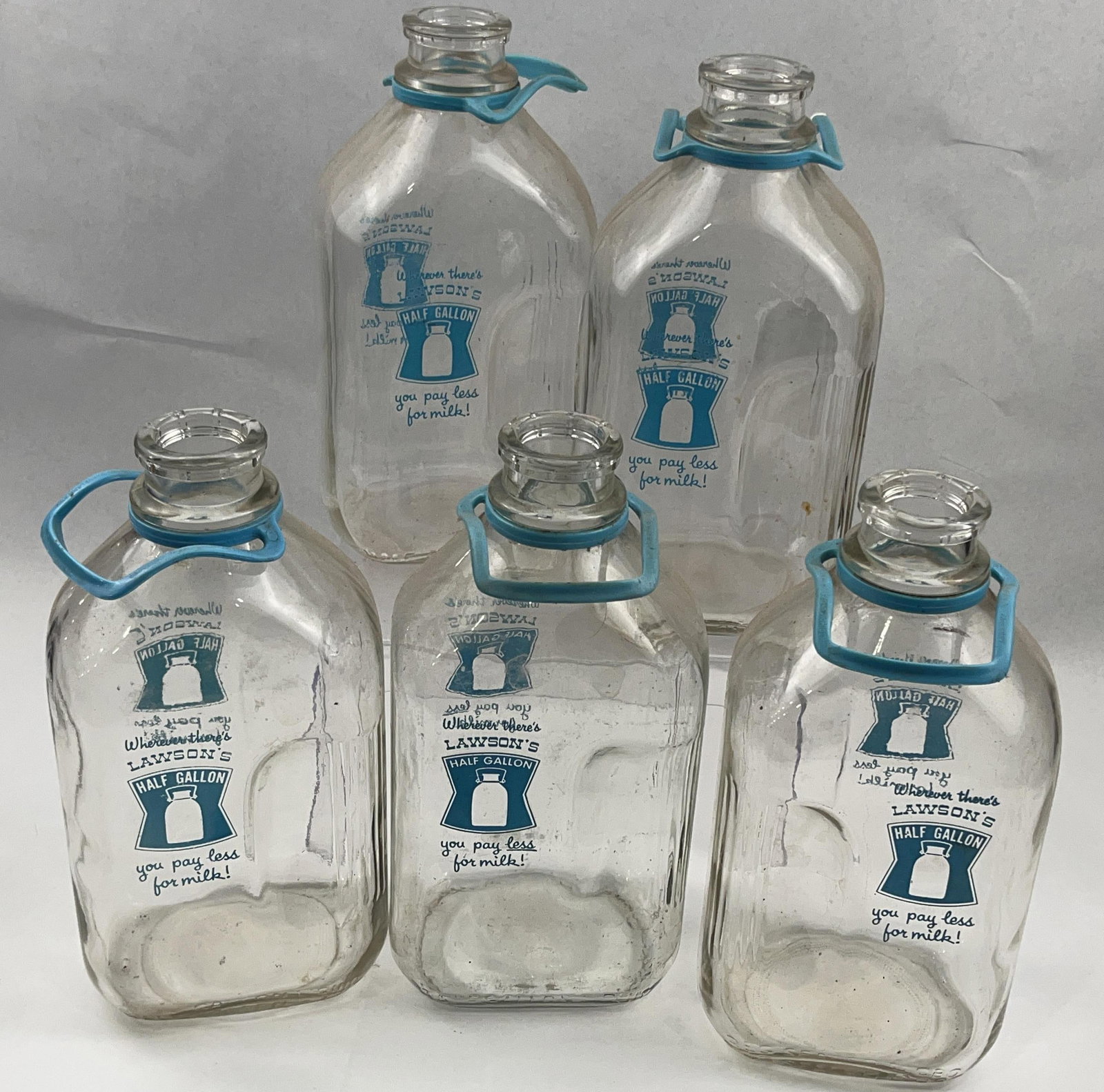 Set 5 Vtg Lawson's Glass Milk Bottles: This set of five American mid-century dairy advertising bottles is constructed from clear glass with blue applied color labels. Each half-gallon bottle features a square form with rounded corners and 
