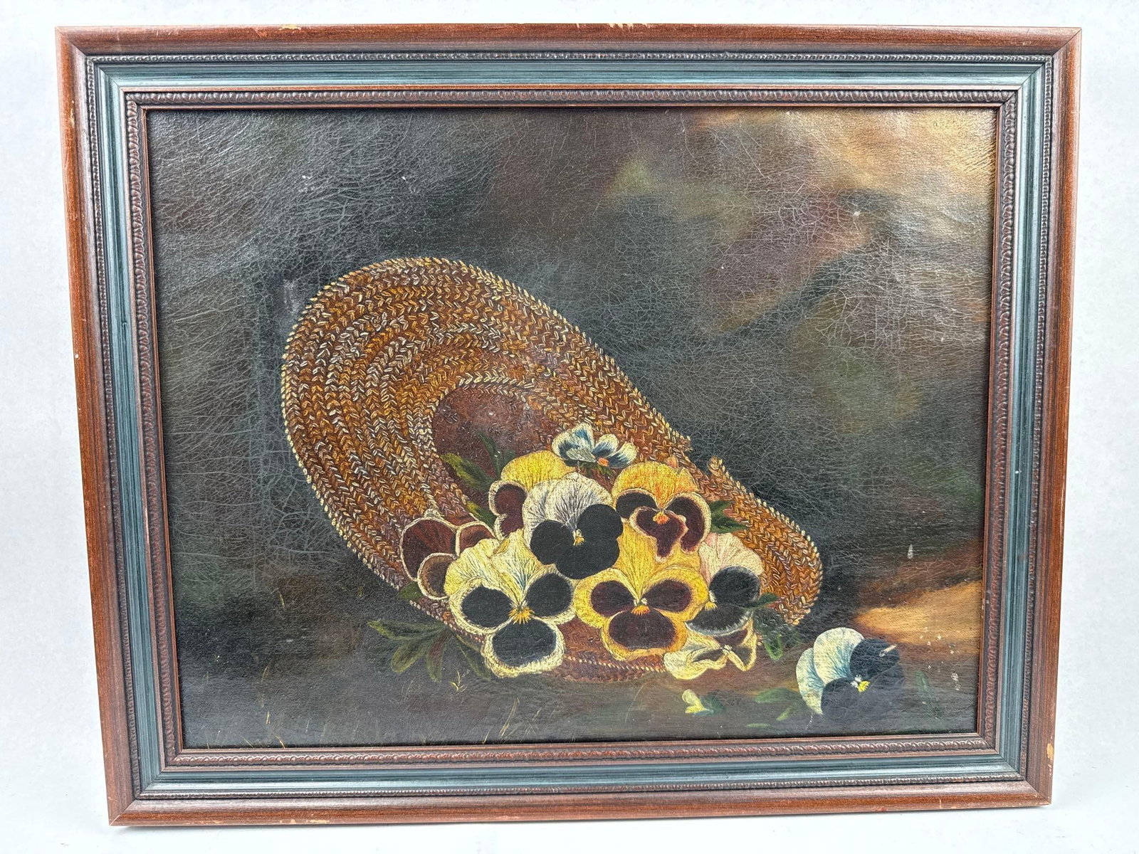 Pinkham Pansies in a Straw Hat O/C: This Victorian-style still life is executed in oil on canvas and depicts an overflowing arrangement of yellow, purple, and white pansies nestled within a woven straw sun hat. The canvas is mounted on