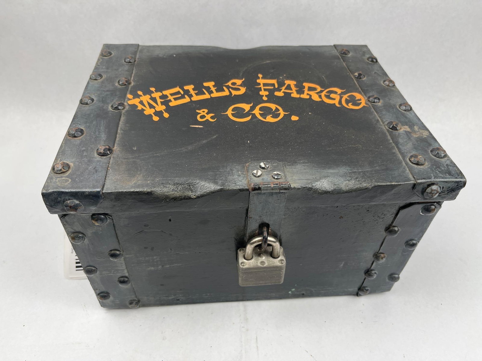 Wells Fargo & Co. Painted Wood and Metal Bound Strongbox: A rectangular wood strongbox featuring a black painted finish and reinforced with metal strapping and domed rivets. The top of the lid features stenciled orange-yellow painted text reading WELLS