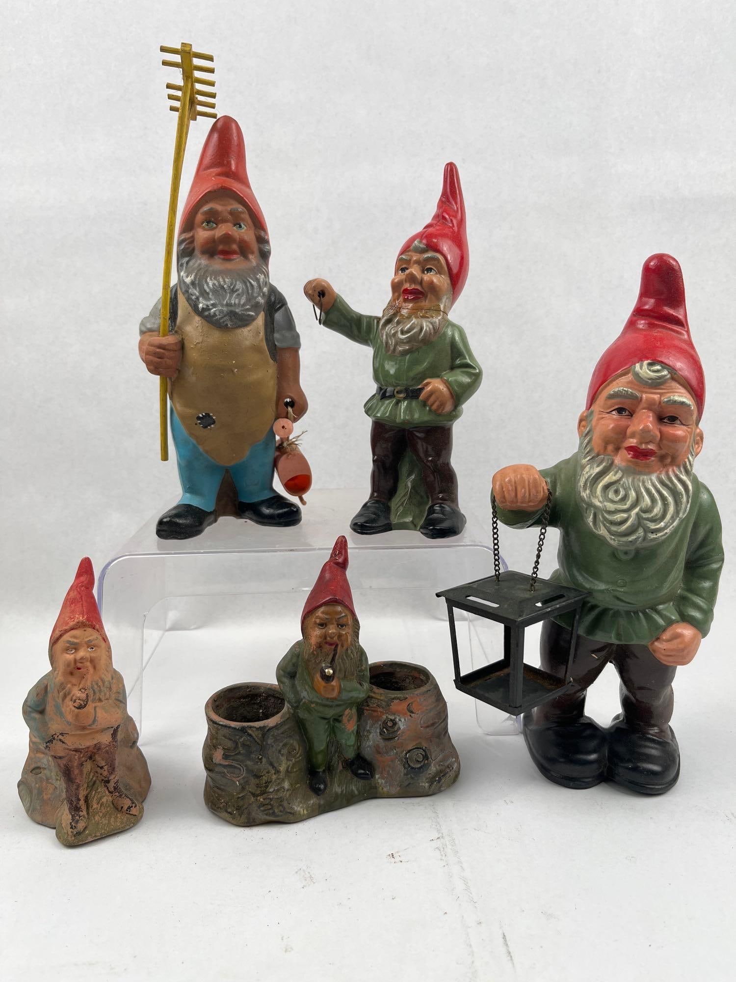 Terracotta & Ceramic Garden Gnomes: This collection features a group of garden gnome figurines constructed from painted terracotta and ceramic. One large figure is depicted wearing a tall red hat and a green tunic, holding a black