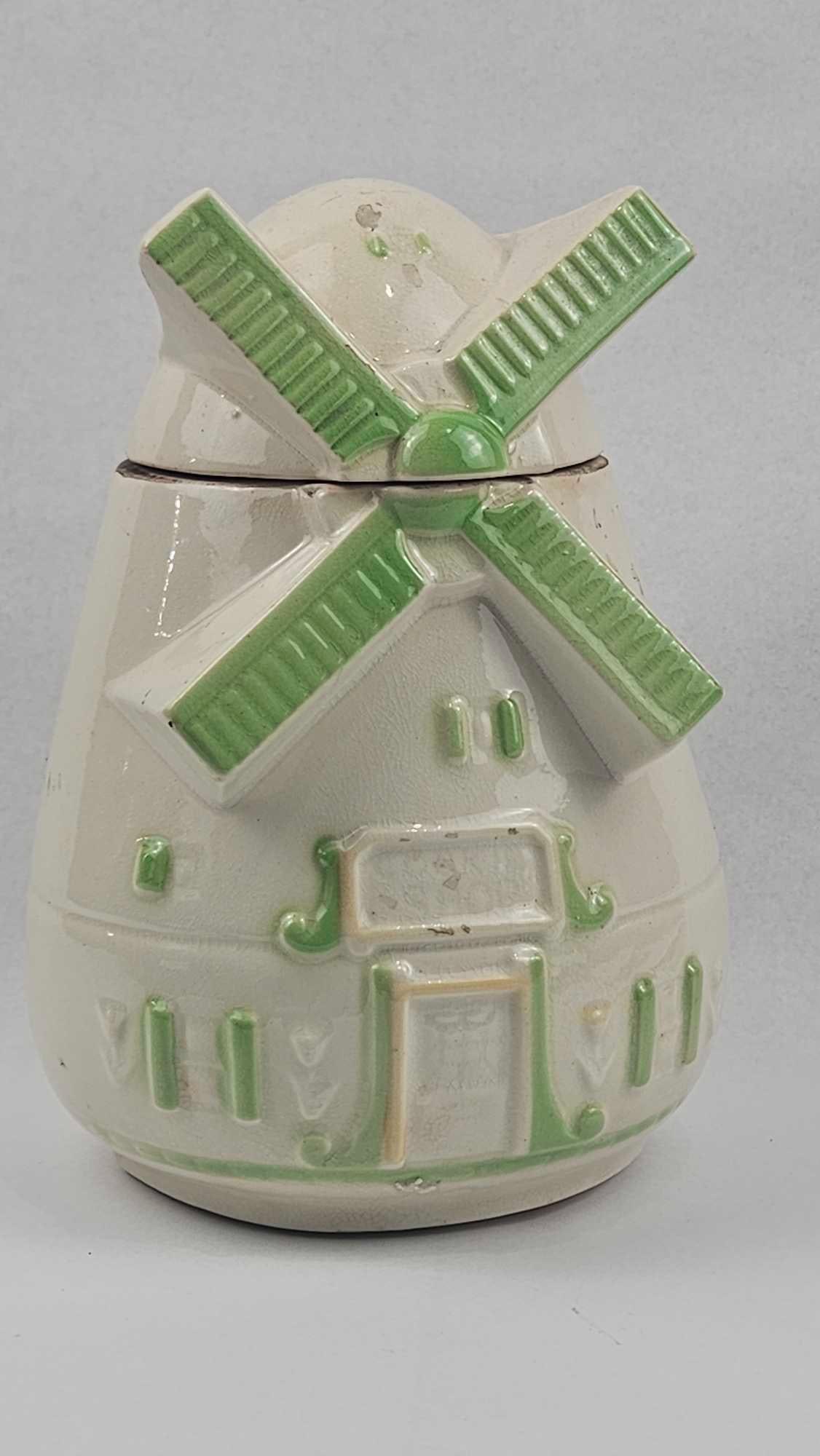 Ceramic Windmill Form Cookie Jar: A vintage ceramic cookie jar modeled in the form of a Dutch windmill. The piece is constructed in two sections, featuring a tapered body and a removable lidded top that comprises the upper structure a