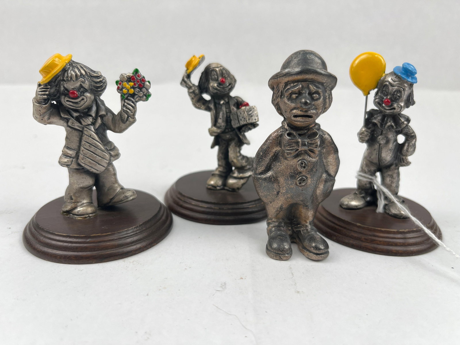 Cast Pewter Clown Figurines w/ Enamel: This group consists of miniature cast pewter figurines depicting various clown characters. The assortment includes a clown holding a yellow enamel balloon and wearing a blue hat, a clown wearing a