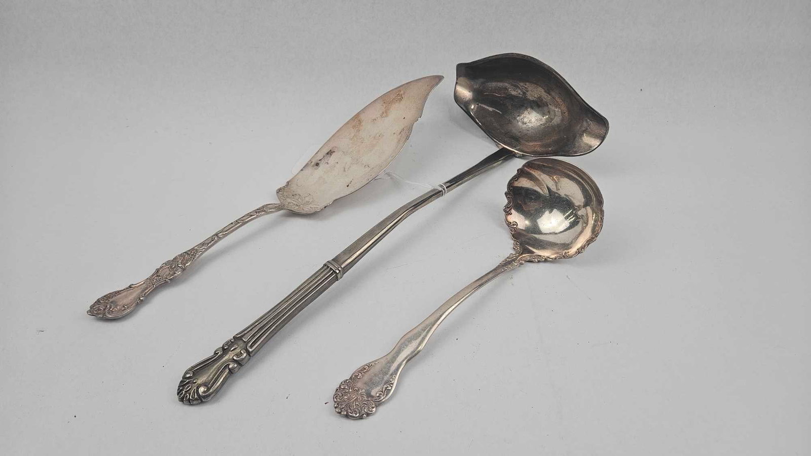 R. Wallace & Sons Silver-Plated Trio: A trio of silver-plated serving pieces comprising a server with a leaf-shaped blade, a large ladle featuring a side-pour spout, and a small ladle with a scalloped bowl. The server and the small ladle