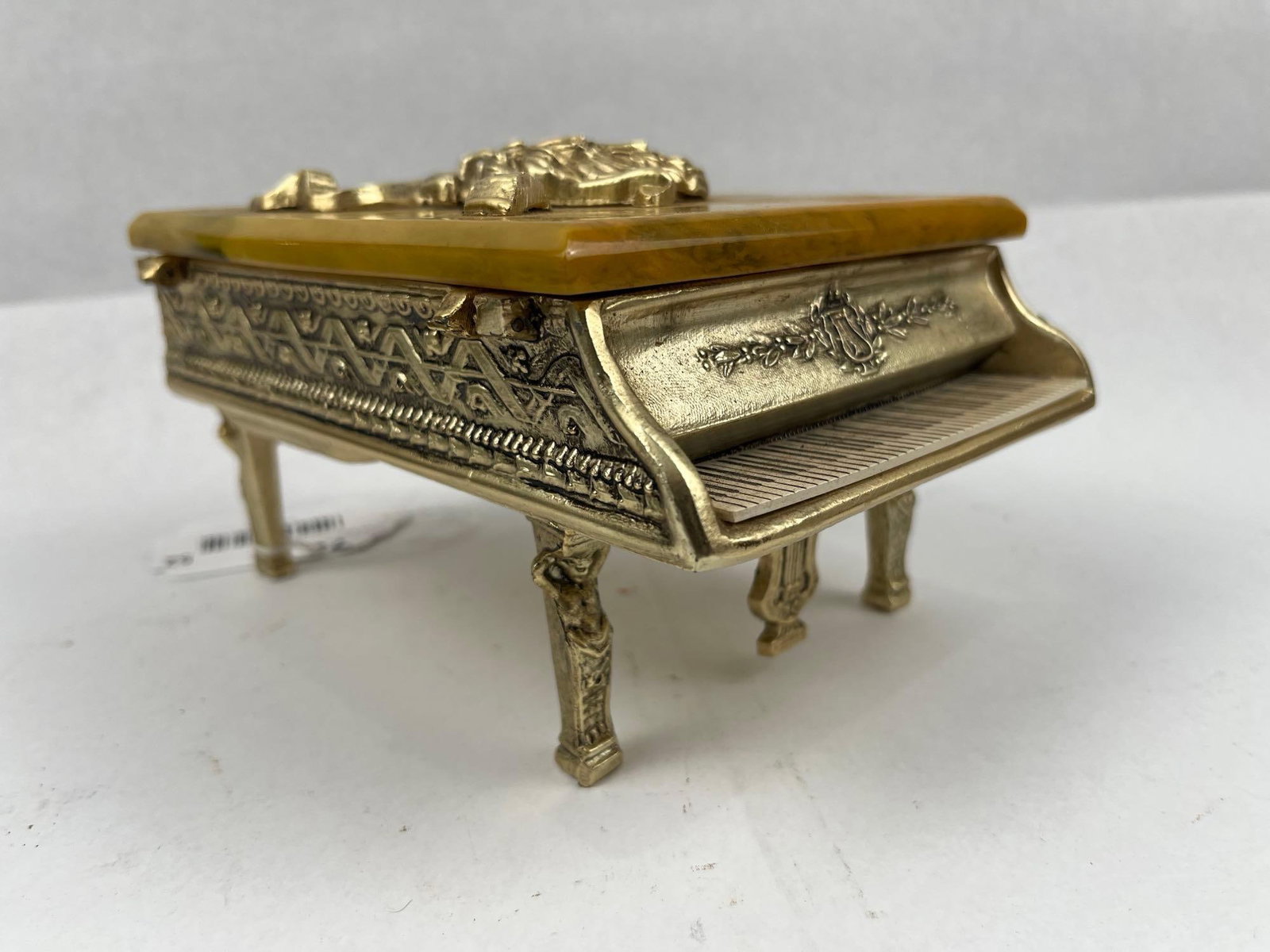 Thorens Swiss Gilt Piano Music Box: A Swiss-made miniature grand piano music box featuring a cast-metal body with a textured gold-tone finish. The exterior is decorated with relief-molded scrollwork, geometric friezes, and an ornate lyr