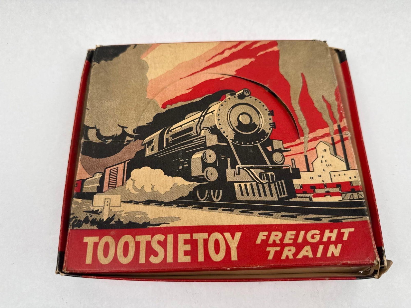 Tootsietoy Die-Cast Freight Train Boxed: A set of five die-cast metal toy train vehicles housed in their original illustrated cardboard box. The set includes a dark gray steam locomotive, a matching coal tender, an orange boxcar, a silver ta