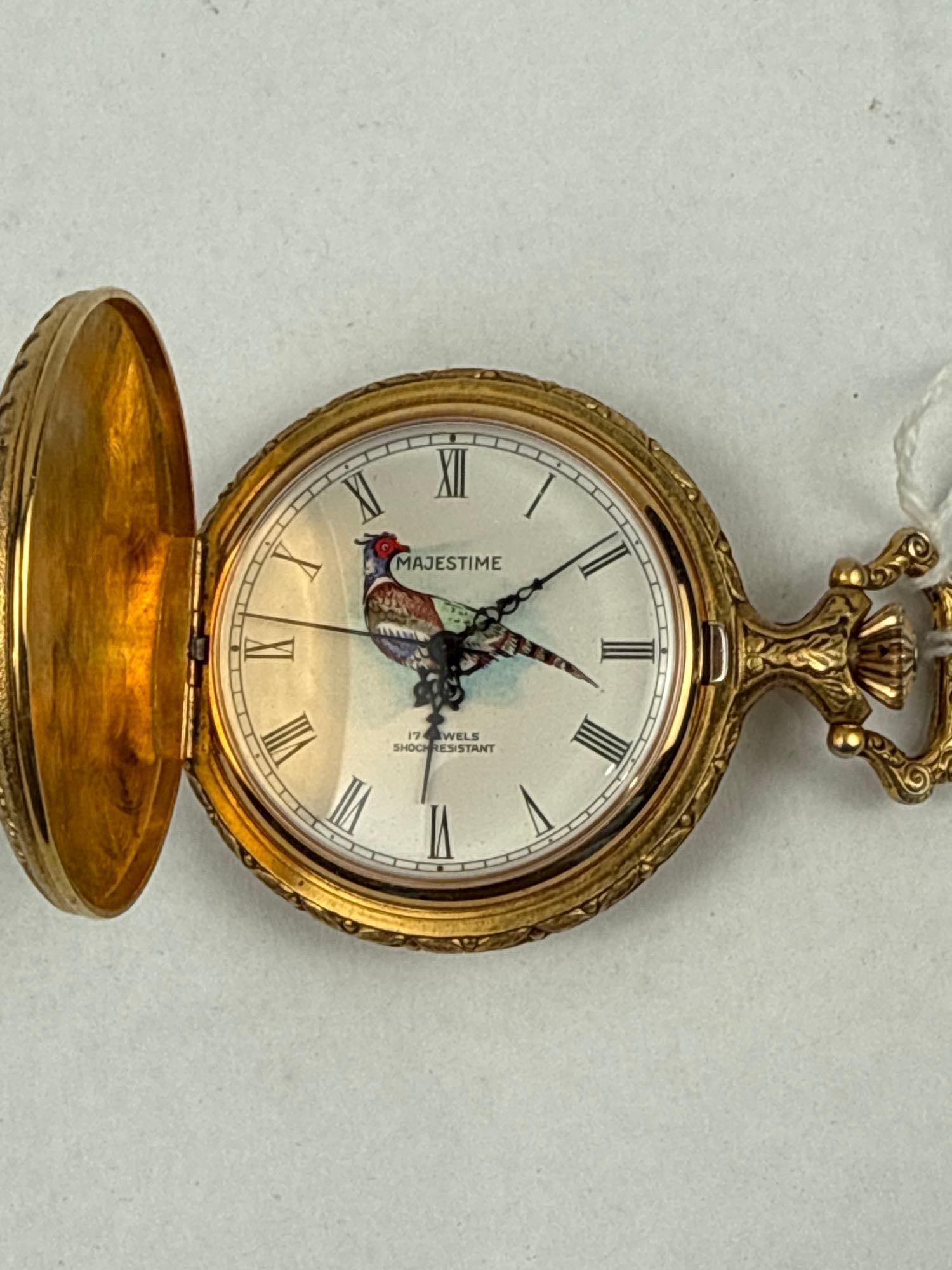 Majesti Swiss Sporting Hunter Watch: This Swiss mechanical hunter-case pocket watch features a gold-tone base metal case decorated with embossed hunting scenes. The front cover depicts a stag in a mountain landscape, while the back