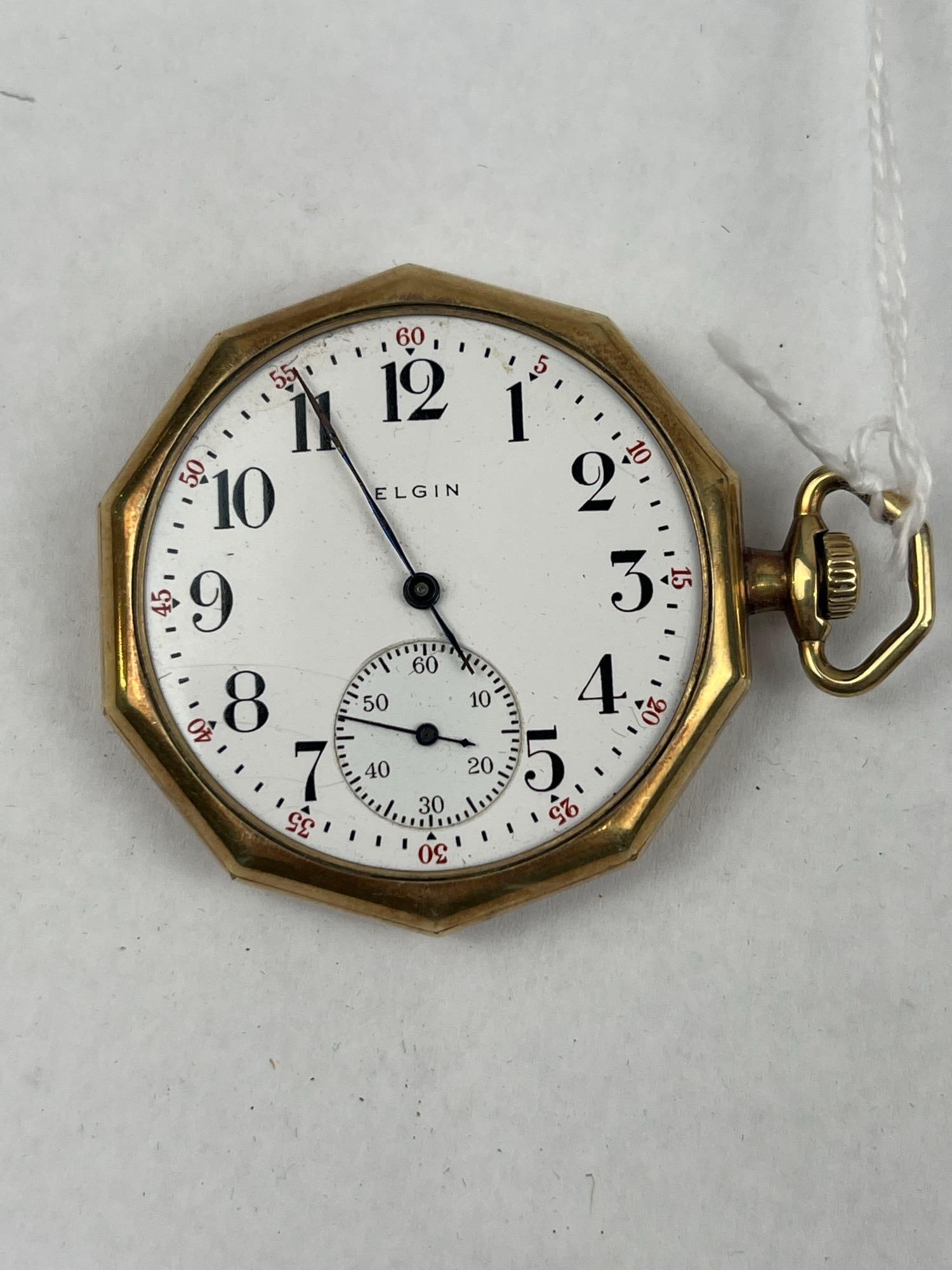 Elgin Octagonal Open-Face Pocket Watch: An American open-face pocket watch featuring a Wadsworth octagonal case in 14 karat yellow gold-filled metal. The white enamel dial is printed in black with the name ELGIN and features black Arabic nu