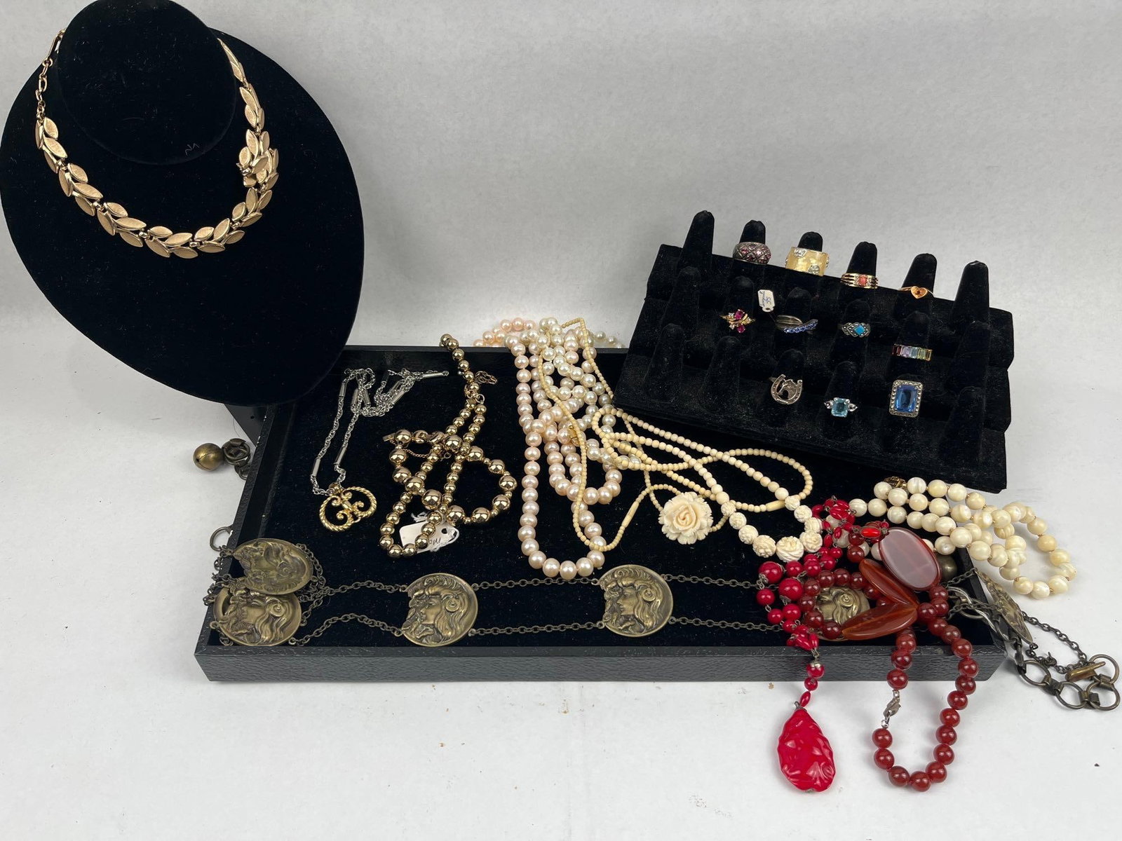 Estate & Costume Jewelry Assortment: A collection of costume and fashion jewelry featuring various necklaces and rings. The group includes a gold-tone necklace composed of textured leaf-shaped links with a matte finish. A white metal
