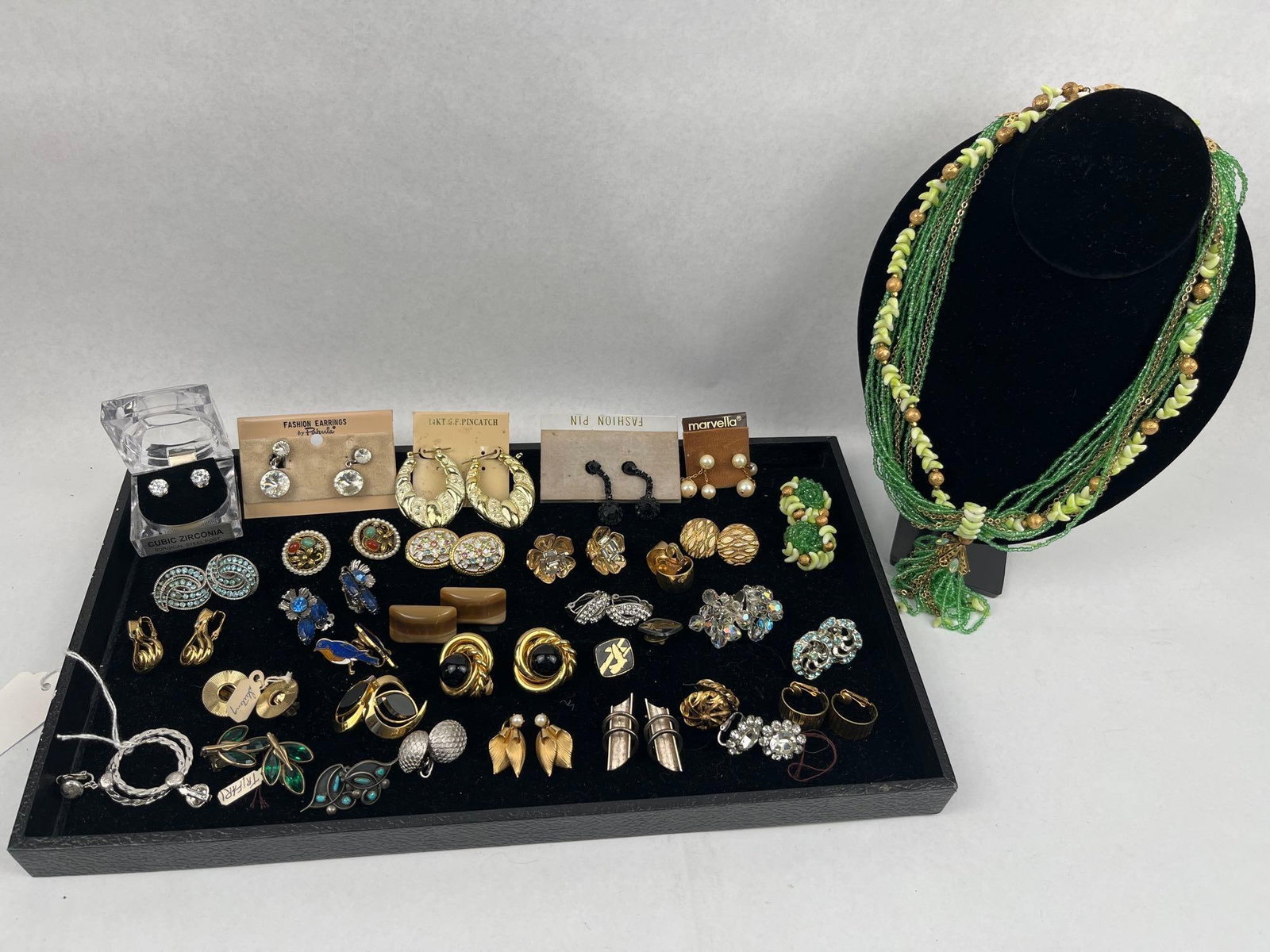 Trifari, Marvella & Pakula Jewelry: A diverse collection of vintage costume jewelry, featuring necklaces, brooches, pins, and numerous pairs of clip-on and stud earrings. Notable among the lot is a multi-strand green seed bead necklace