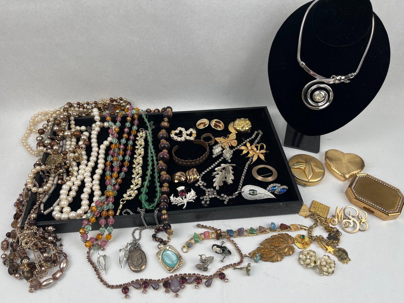 Costume Jewelry & Vanity Compacts: This lot contains a large variety of costume jewelry and vanity accessories. Included are three gold-tone compacts: a heart-shaped piece with a sunburst engine-turned pattern, a circular piece with a 