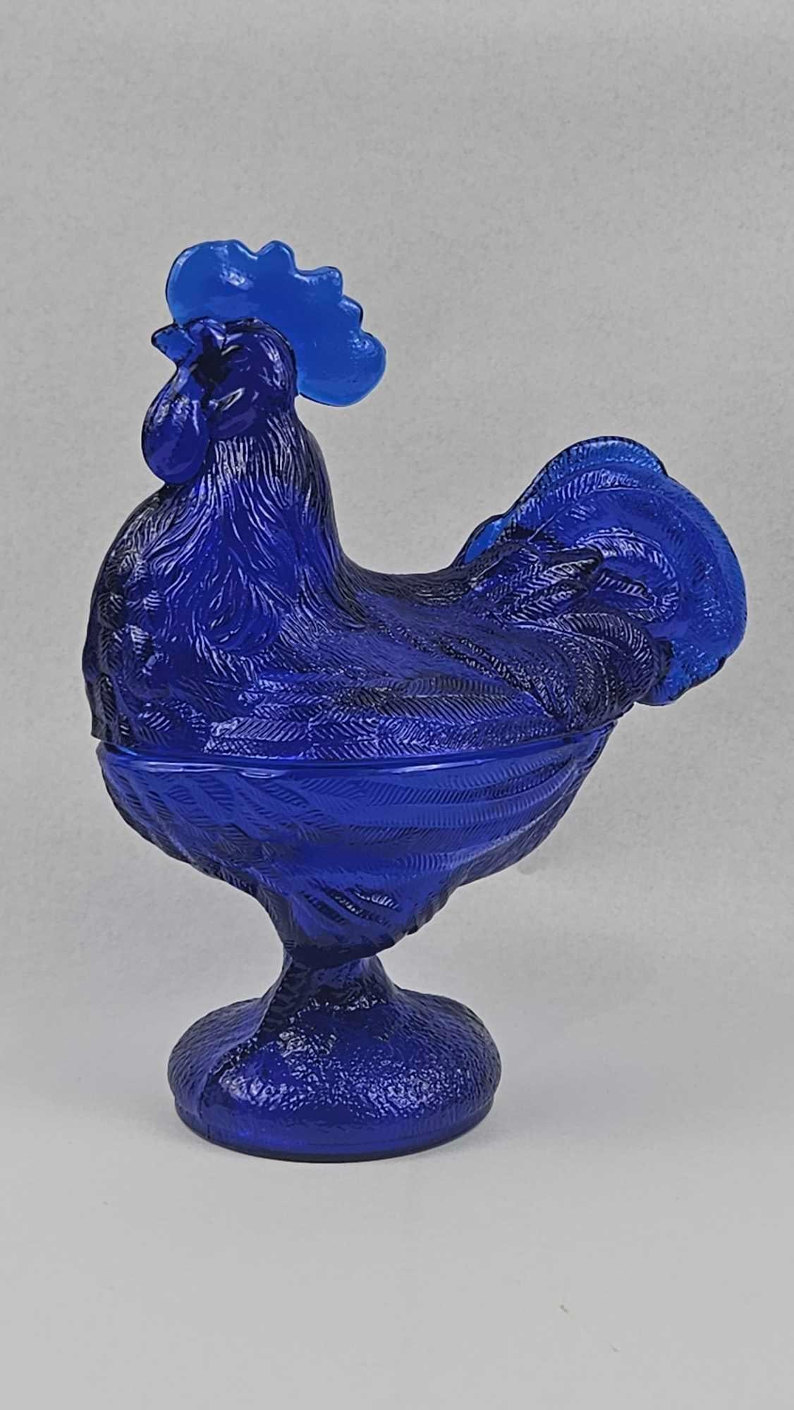 Cobalt Blue Glass Rooster Covered Dish: A two-piece decorative object crafted from cobalt blue pressed glass, featuring a standing rooster lid and a matching footed base. The upper section is molded in the form of a rooster with intricate