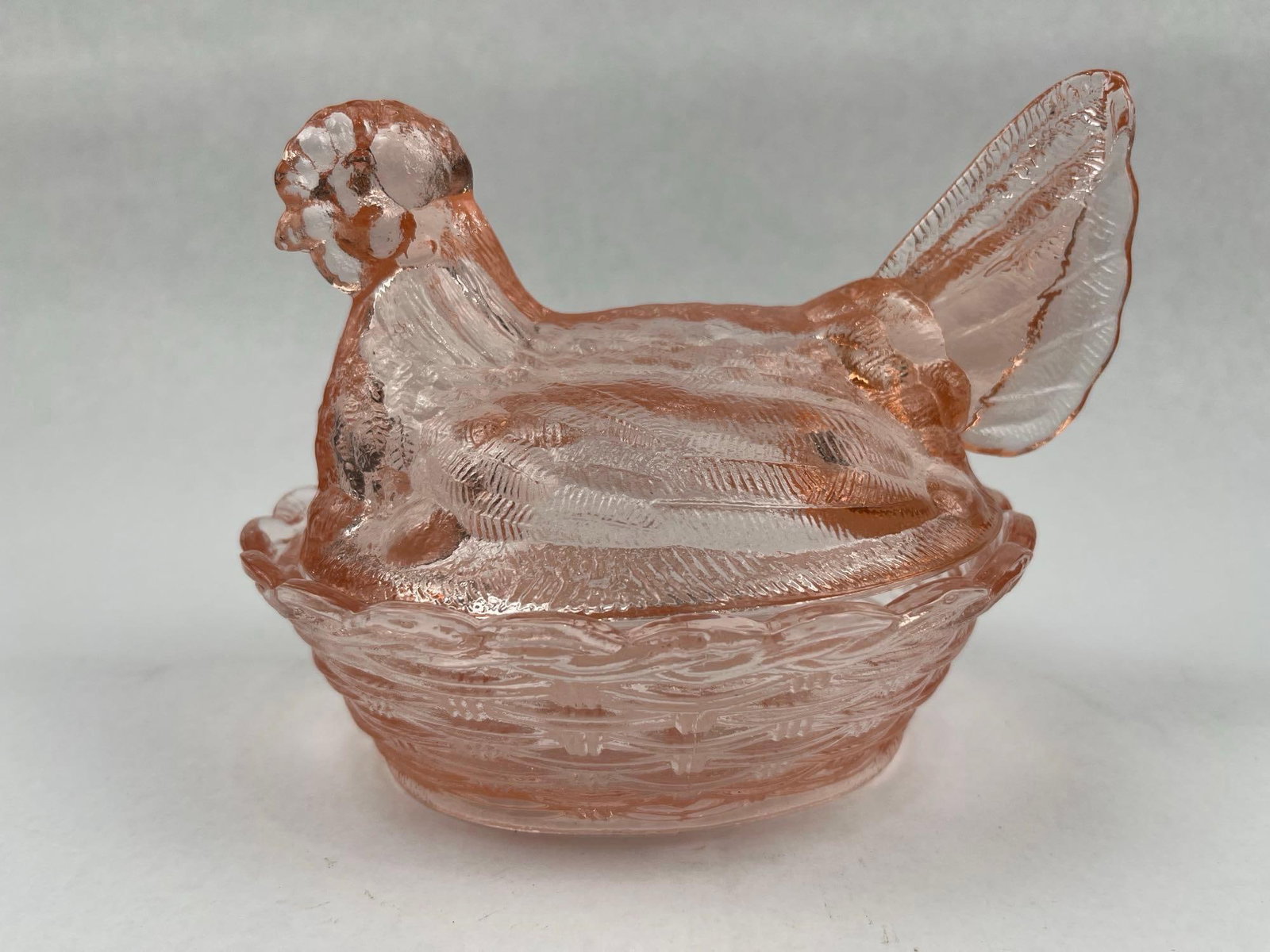 Pink Pressed Glass Hen on Nest Dish: A two-piece American pink pressed glass covered dish in the form of a hen on a nest. The set consists of a figural lid depicting a nesting hen with molded feather texture and an upright tail,