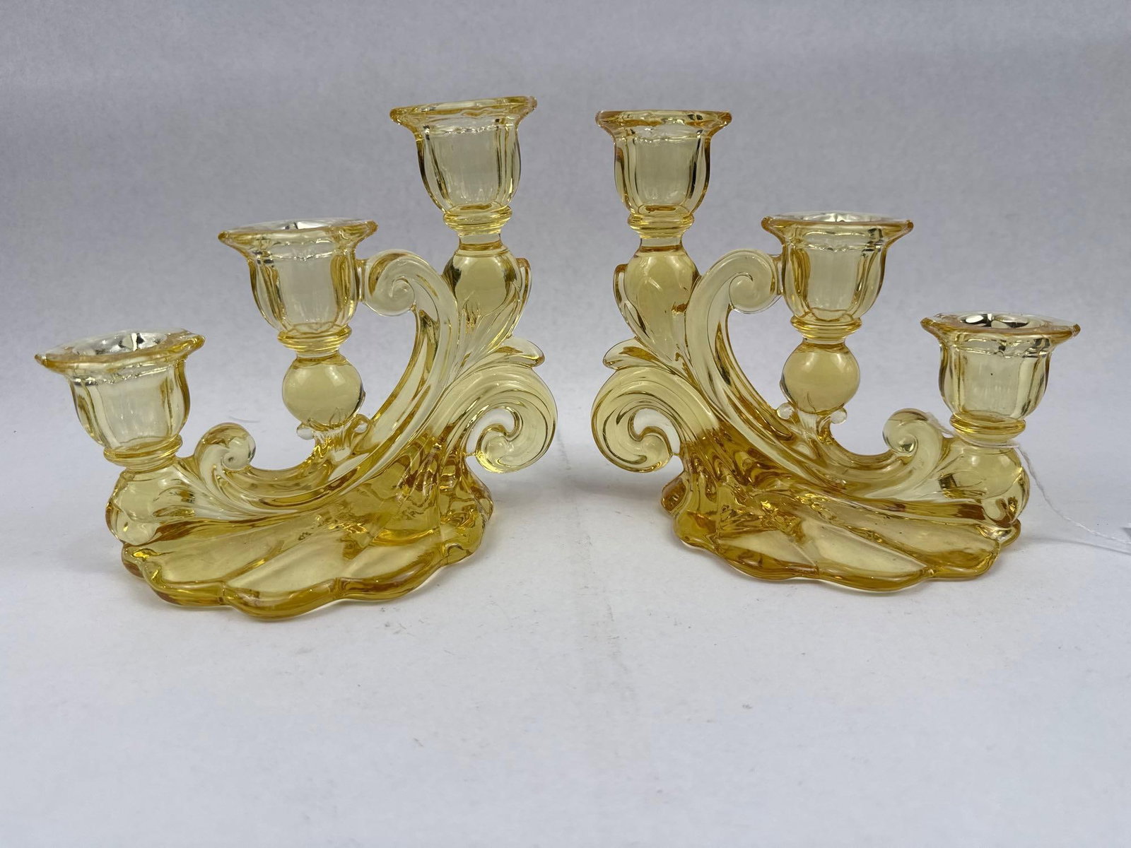 Pair Yellow Three-Light Candelabra: A pair of yellow pressed glass three-light candelabra featuring a scrolling asymmetrical design. Each candelabrum is composed of a scalloped shell-form base that supports three C-scroll arms. These