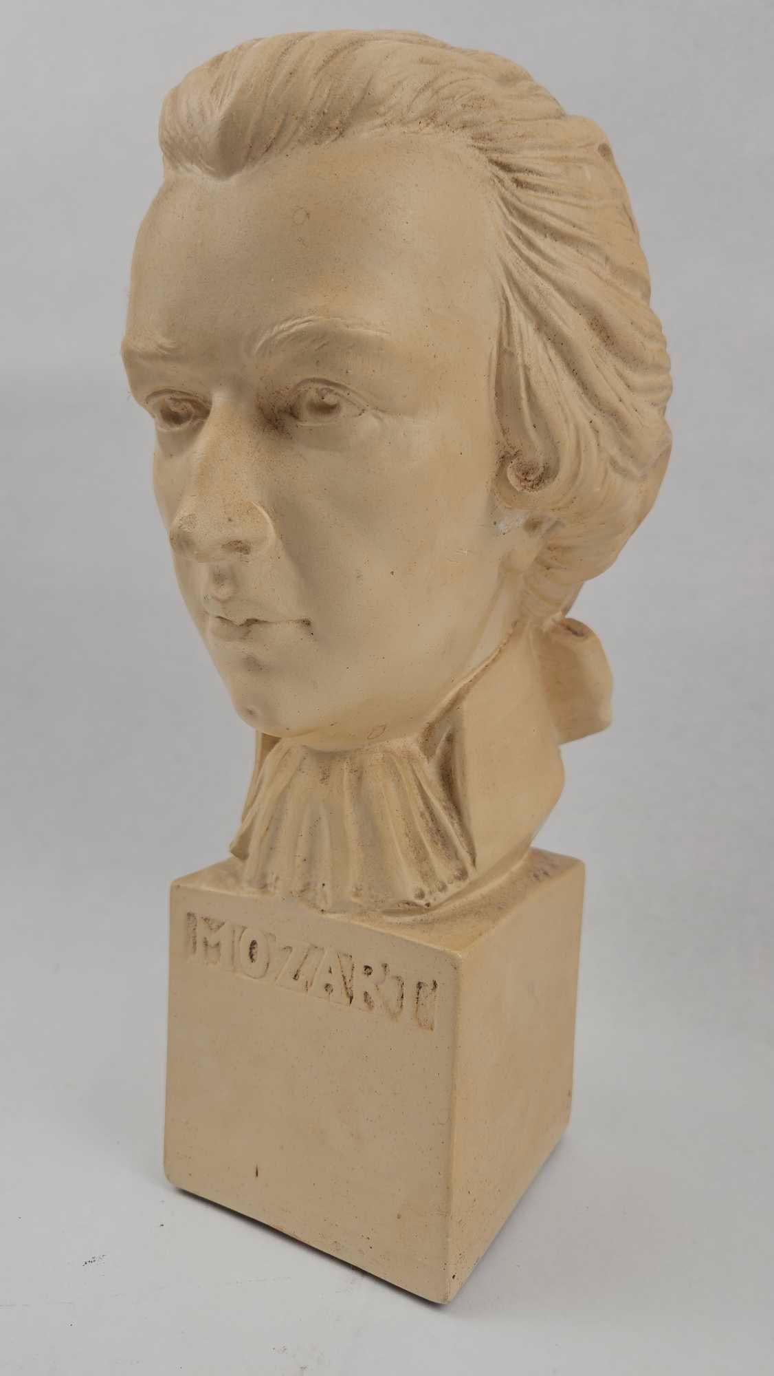 HSCO Products Inc. Mozart Portrait Bust: A portrait bust of Wolfgang Amadeus Mozart, cast in a beige-toned composite material. The composer is depicted in profile and three-quarter views wearing an 18th-century style wig tied with a ribbon