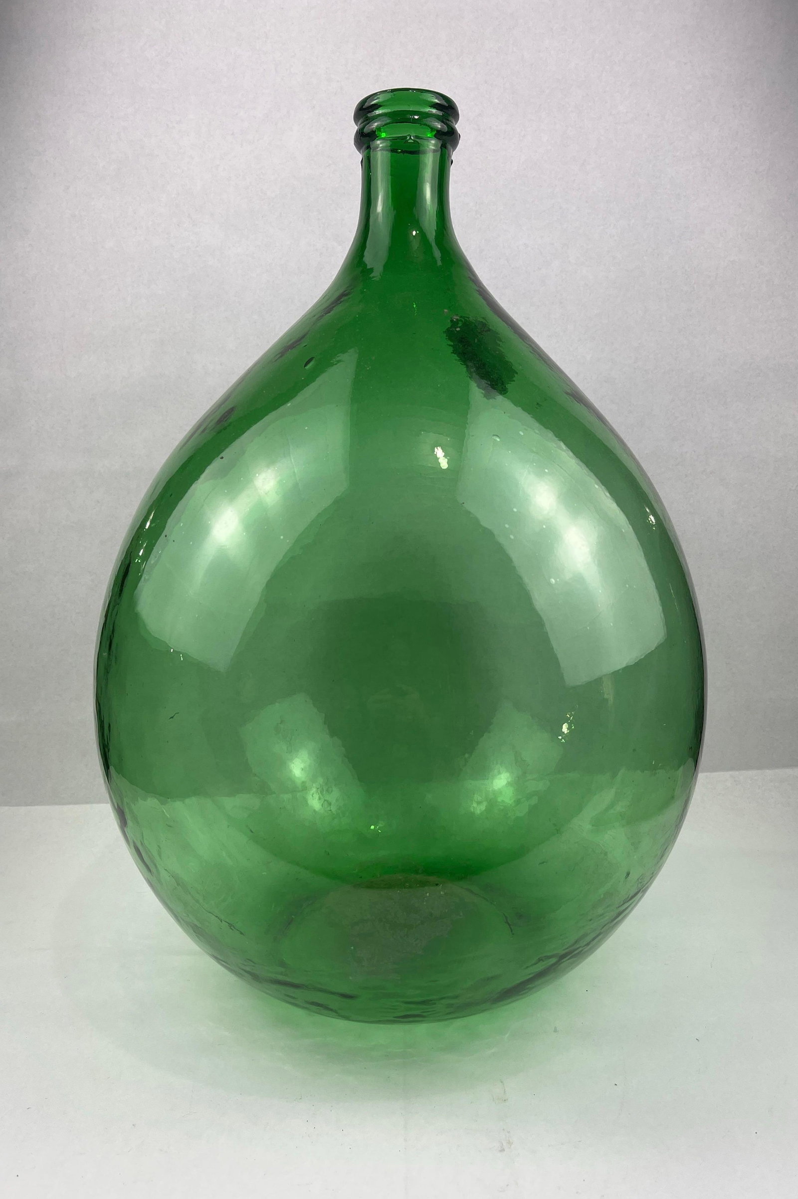European Emerald Green Glass Demijohn: A large glass vessel, commonly referred to as a demijohn or carboy, executed in vibrant, translucent emerald green glass. The bottle features a classic ovoid body that narrows into a slender neck