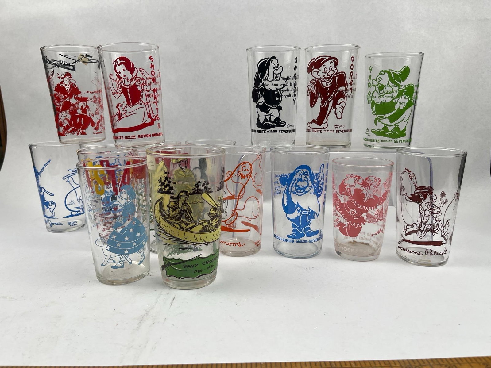 Disney & Pop Culture Enameled Tumblers: An assortment of mid-century glass tumblers featuring screen-printed character illustrations in multi-colored enamels. The collection includes various subjects from the film Snow White and the Seven