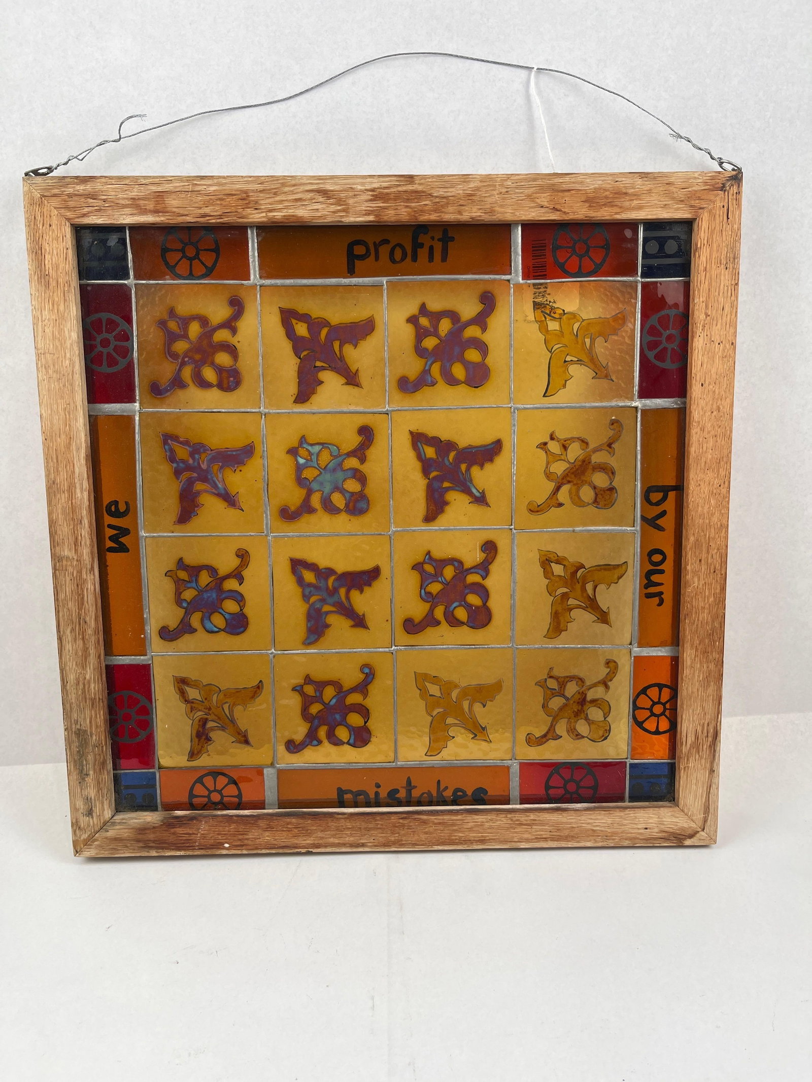 Wood-Framed Stained Glass Proverb Panel: A square leaded stained glass panel housed in a light-colored wood frame. The central field is composed of sixteen square amber-yellow glass tiles arranged in a four-by-four grid. Each tile is